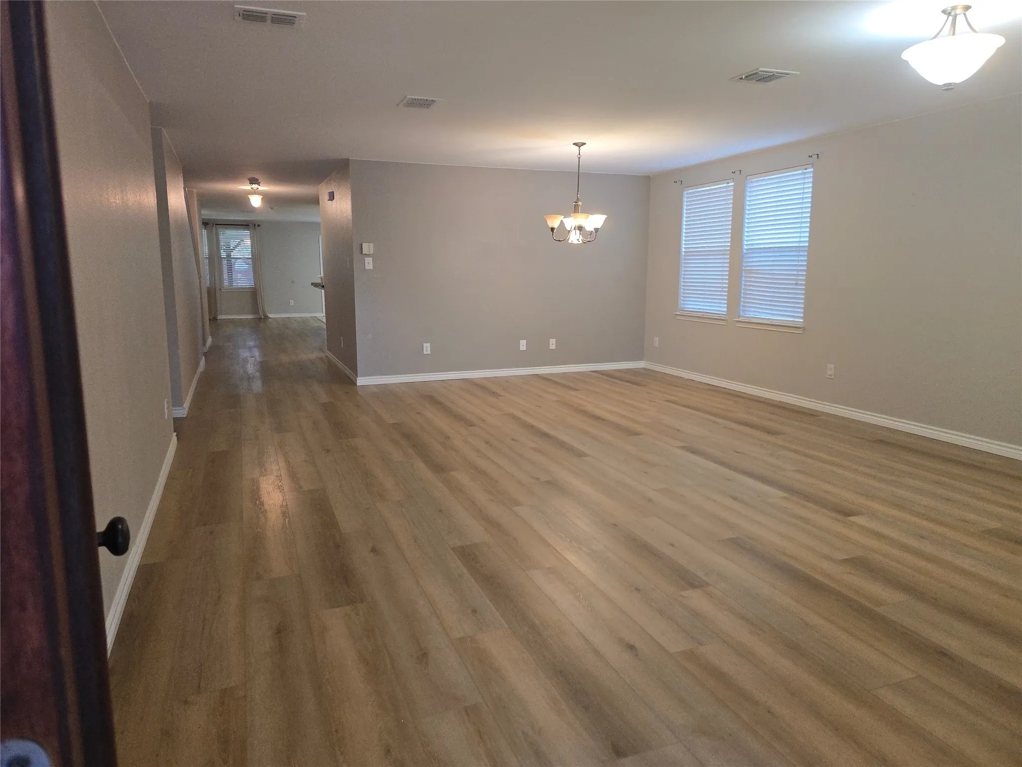 Spacious interior with wood-finish flooring, neutral wall tones, multiple windows with blinds, and ceiling-mounted lighting fixtures