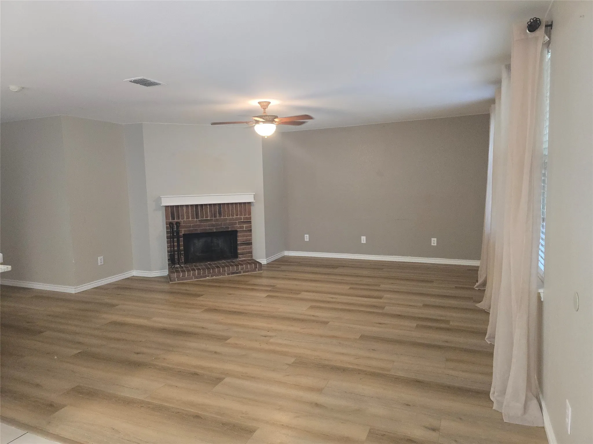 Expansive room featuring wood-finish flooring, a brick fireplace with a white mantel, and a ceiling fan