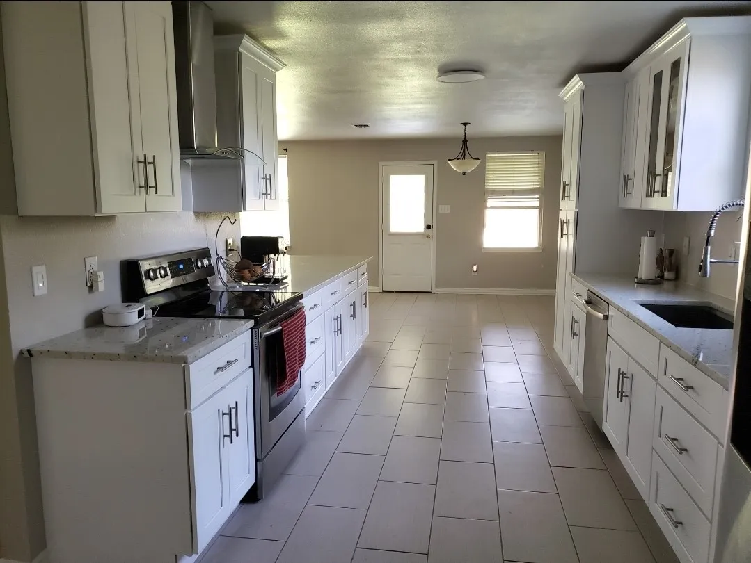 White shaker cabinetry, light-toned countertops, stainless steel appliances, and large format floor tiling