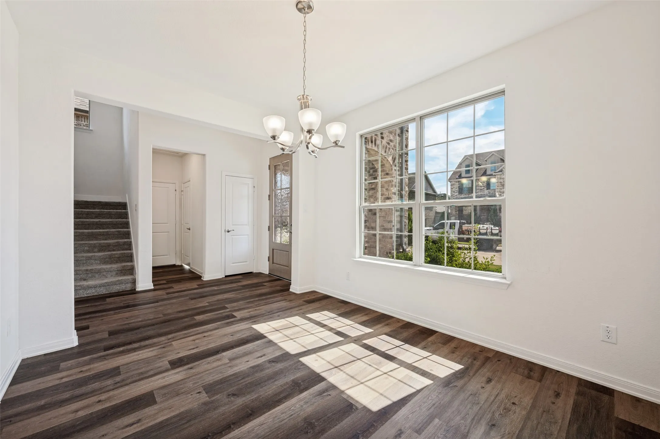Spacious room with dark wood-finish flooring, a large multi-pane window, and a five-light chandelier