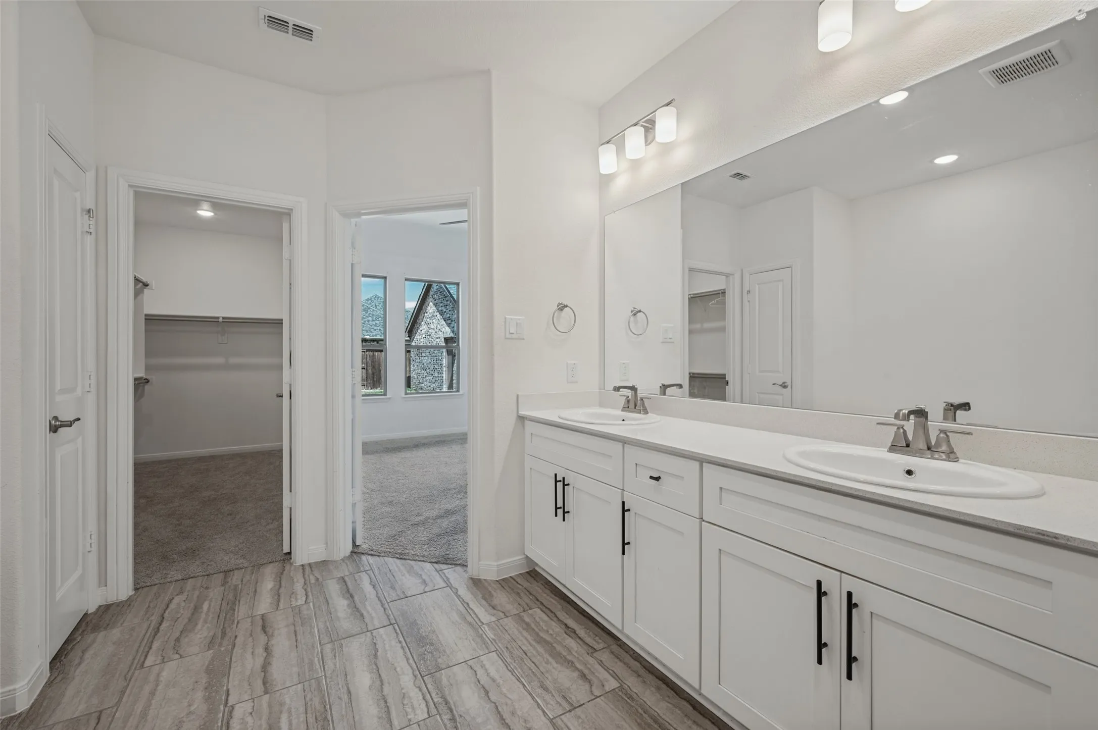 Dual vanity with undermount sinks, stone countertops, large wall-mounted mirror, and tile flooring