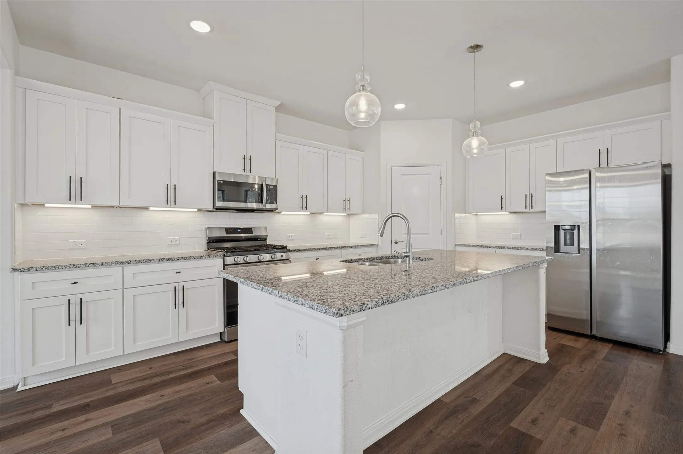 Kitchen featuring white shaker cabinetry, stainless steel appliances, speckled stone countertops, a subway tile backsplash, and wood-finish flooring