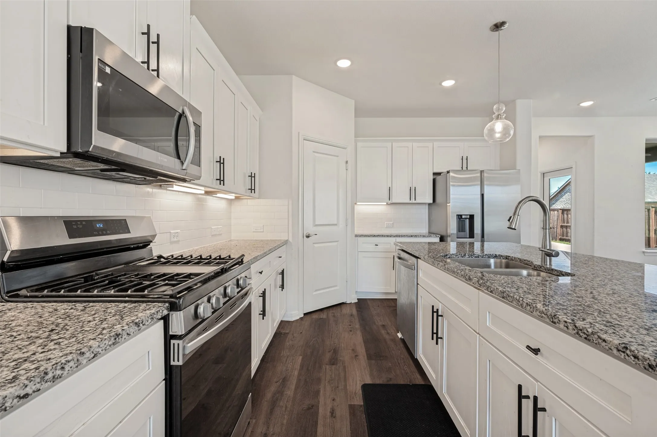 Kitchen featuring white cabinetry, stainless steel appliances, granite countertops, wood-finish flooring, and a subway tile backsplash