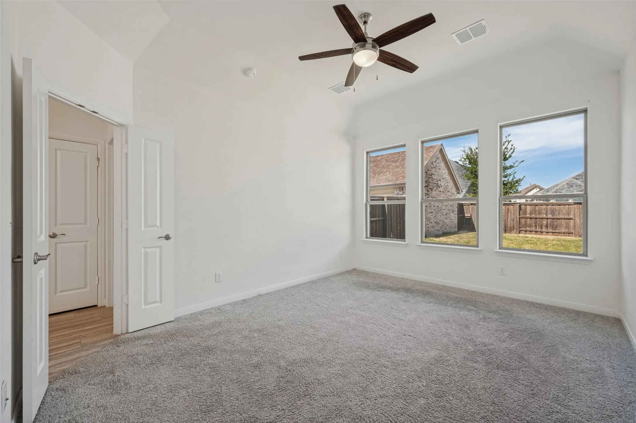 Vaulted ceiling with a contemporary ceiling fan, three large windows, gray carpeting, and white interior doors with satin nickel hardware