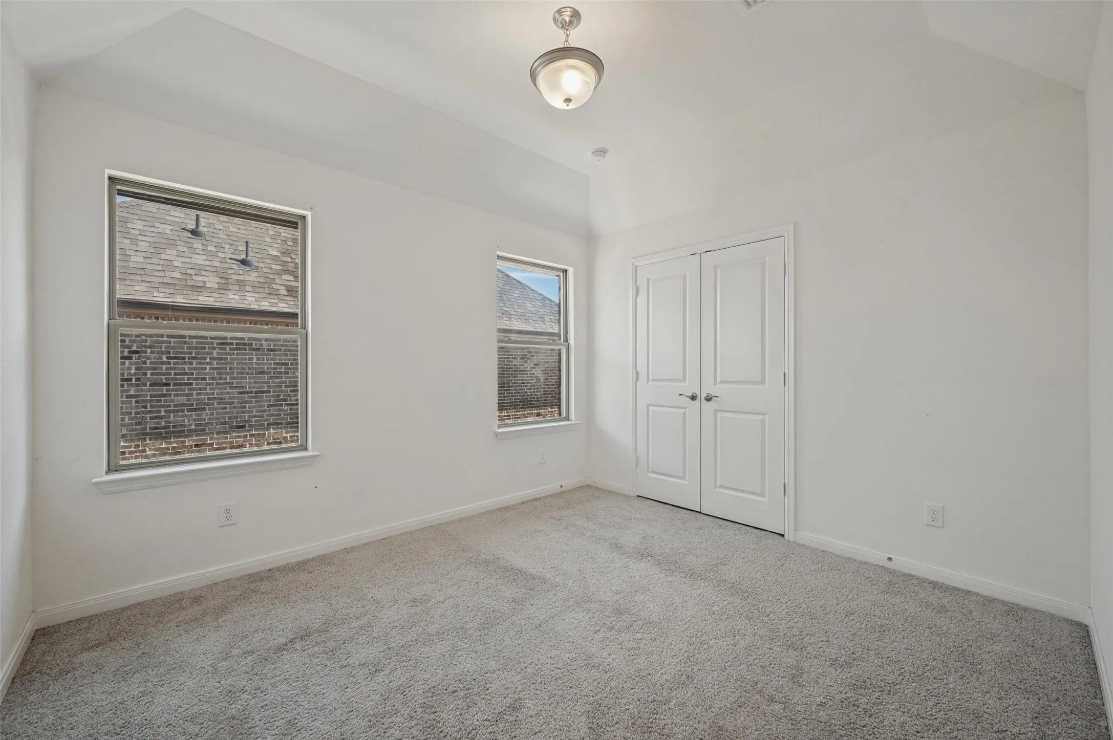 Vaulted ceiling with a flush-mount light fixture, two windows with white trim, gray carpet flooring, and white bifold closet doors