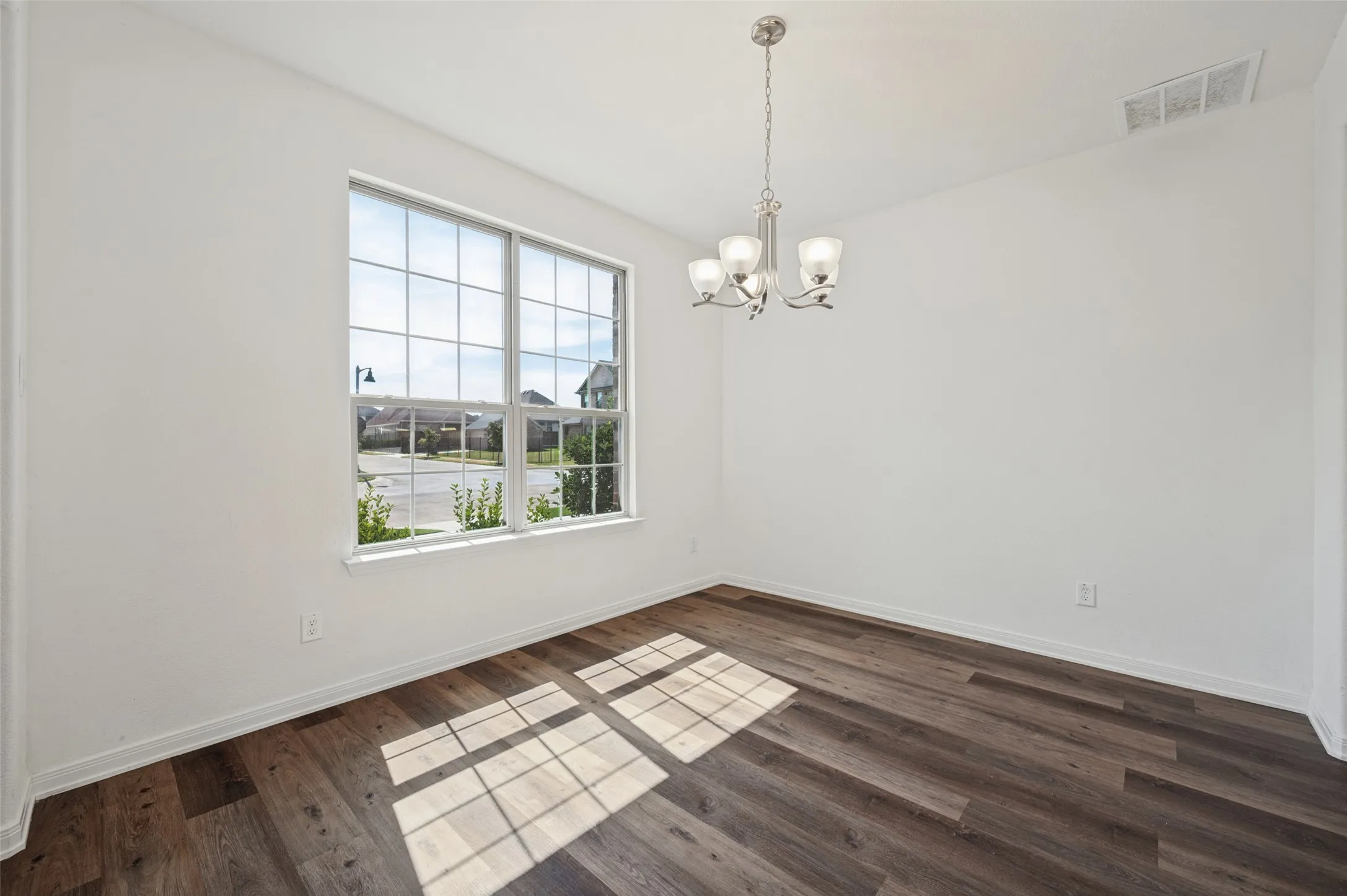 White walls with a single window, wood-finish flooring, and a four-light chandelier