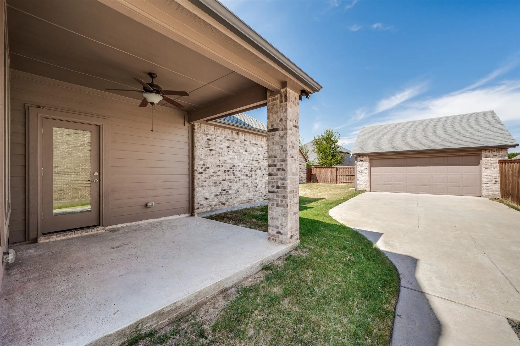 Covered patio with a ceiling fan, brick veneer exterior, and detached garage with a concrete driveway