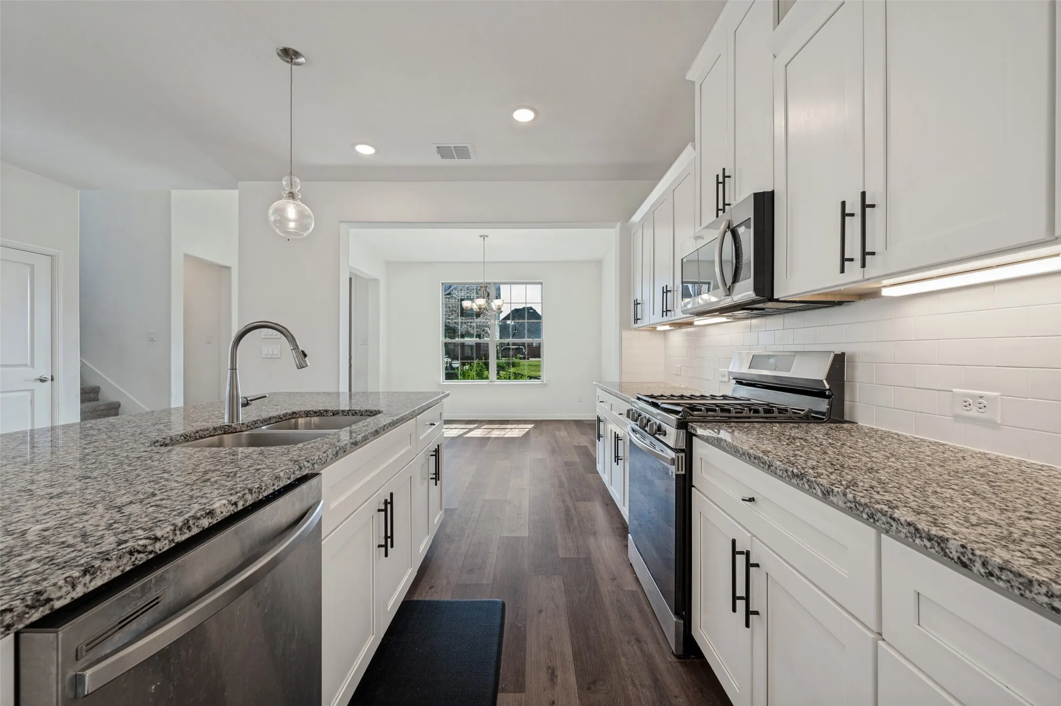 Kitchen featuring white shaker cabinetry, stainless steel appliances, speckled stone countertops, and wood-finish flooring