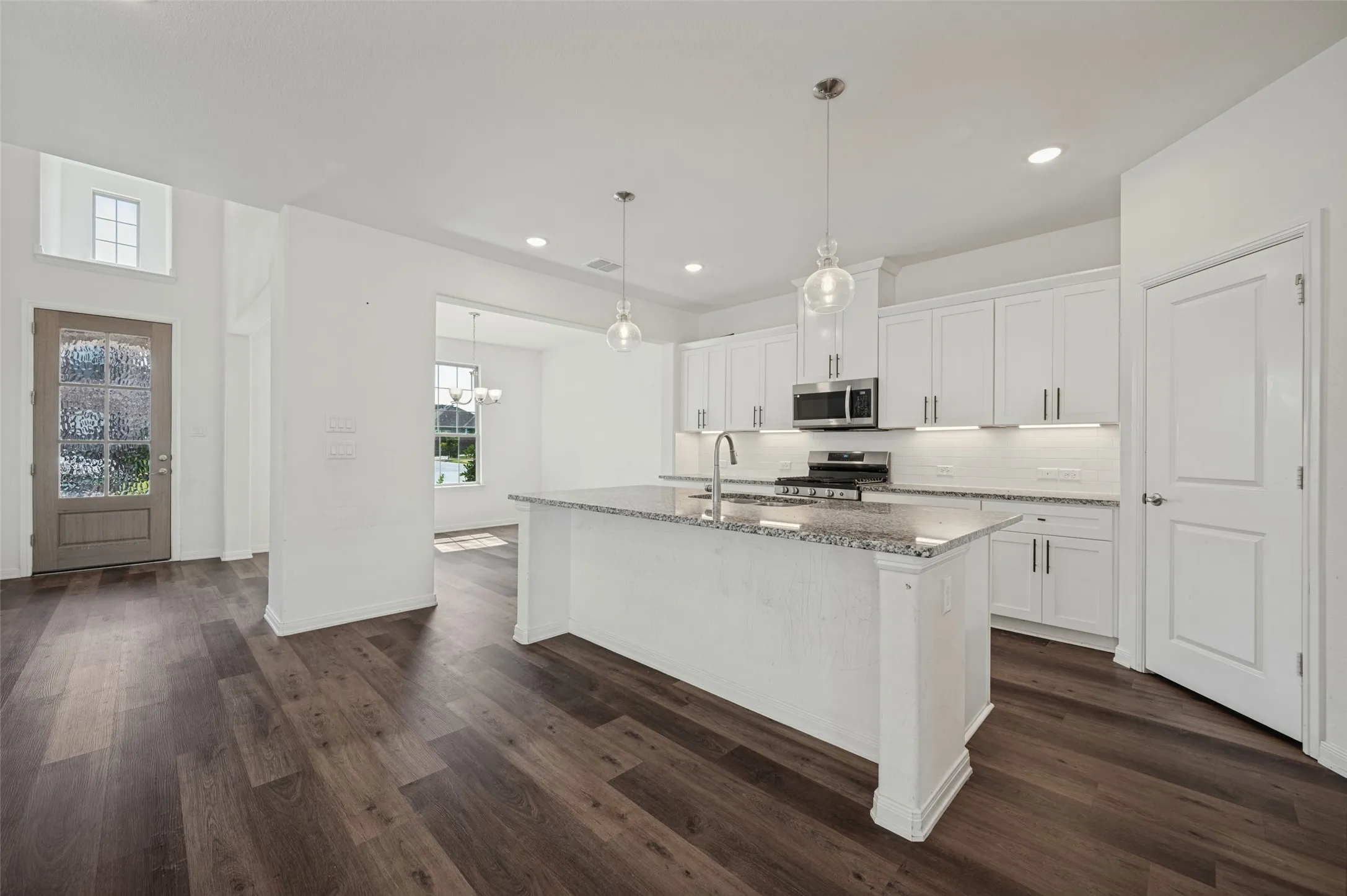 Wood-finish flooring throughout, kitchen featuring white cabinetry, granite countertop island, stainless steel appliances, and pendant lighting