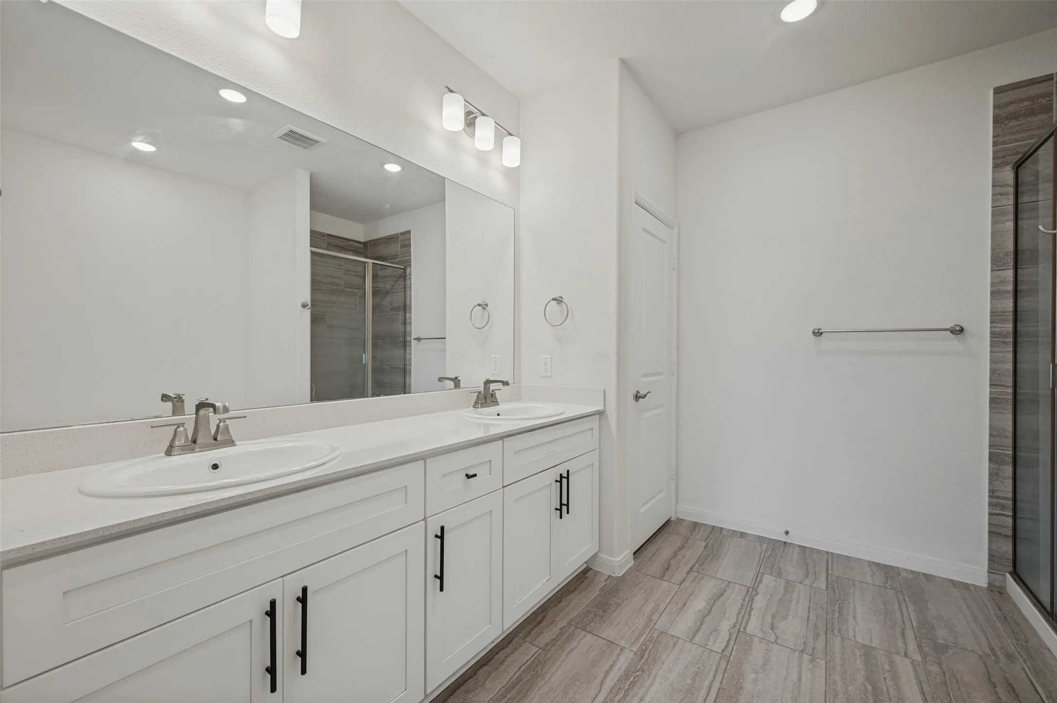 Spacious bathroom featuring a dual vanity with white cabinetry, a large mirror, a glass-enclosed shower, and tile flooring