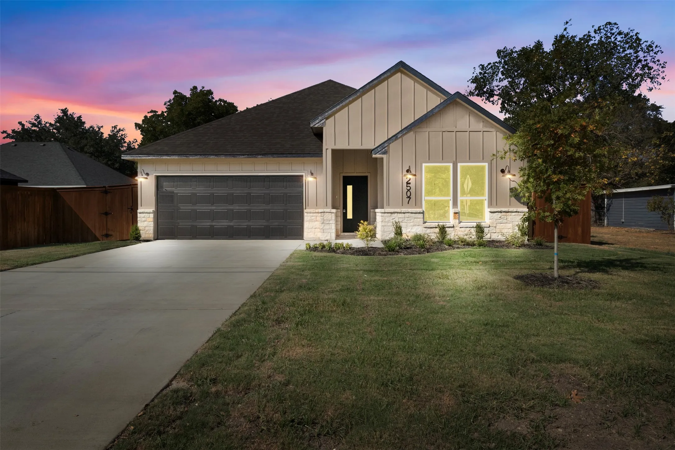 Modern exterior featuring vertical board and batten siding, stone facade accents, a dark-paneled garage door, and a concrete driveway