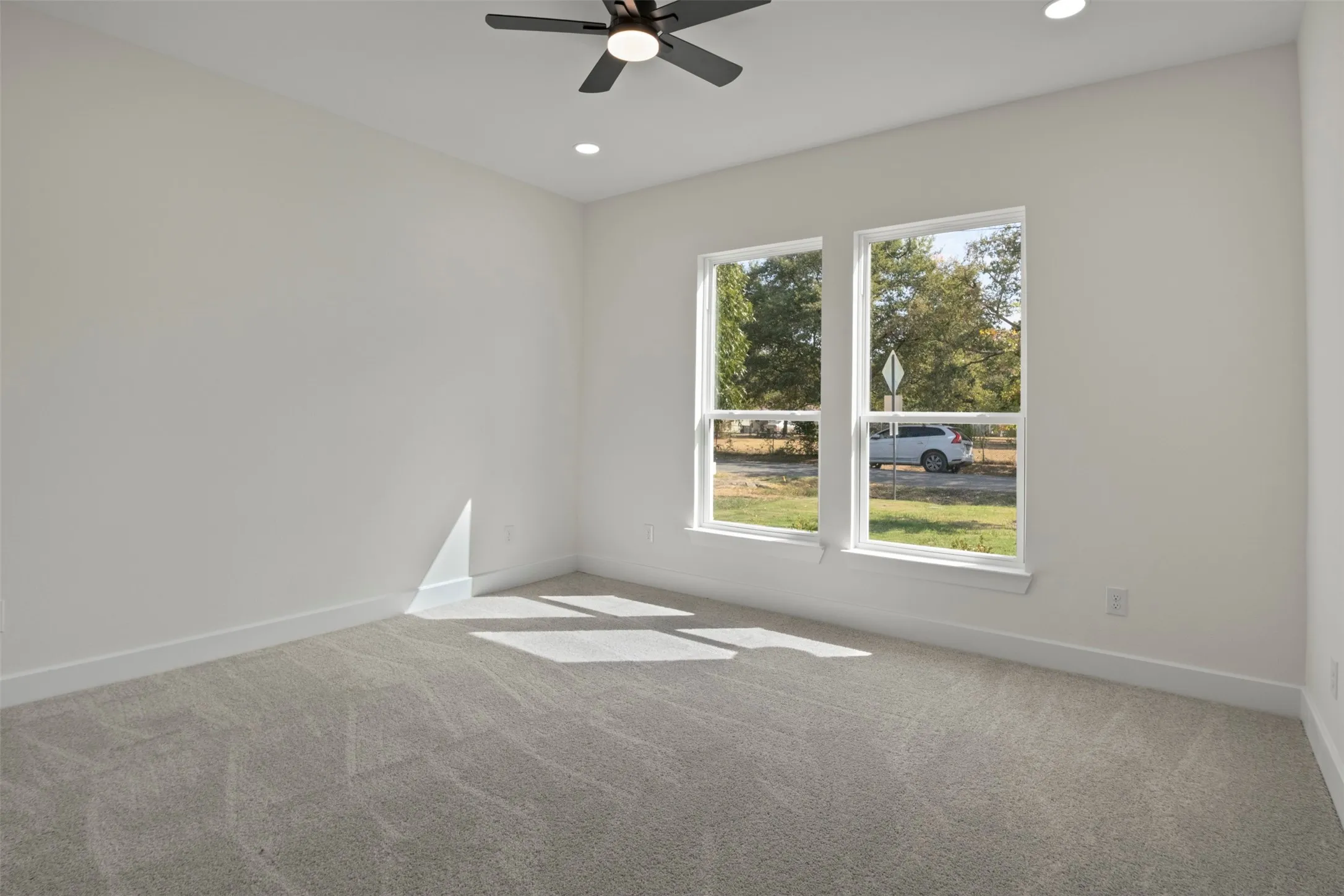 Light gray carpeting, two large windows, white walls, recessed lighting, and a ceiling fan with integrated lighting