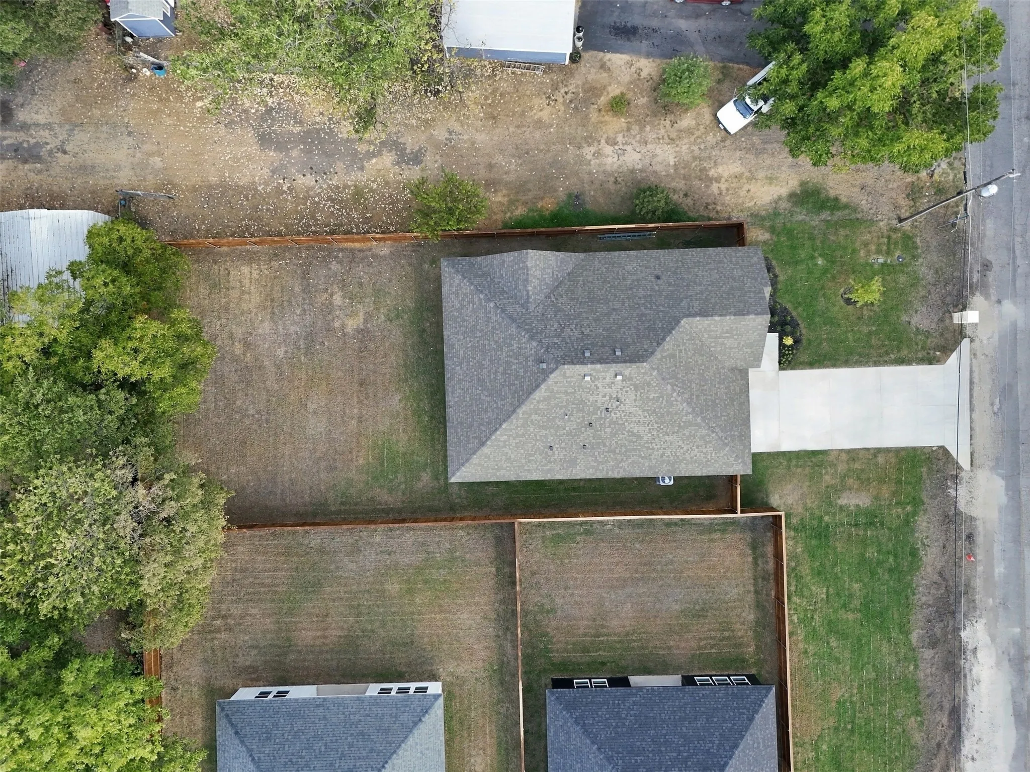New construction residence featuring a gray shingle roof, concrete driveway, and established fencing