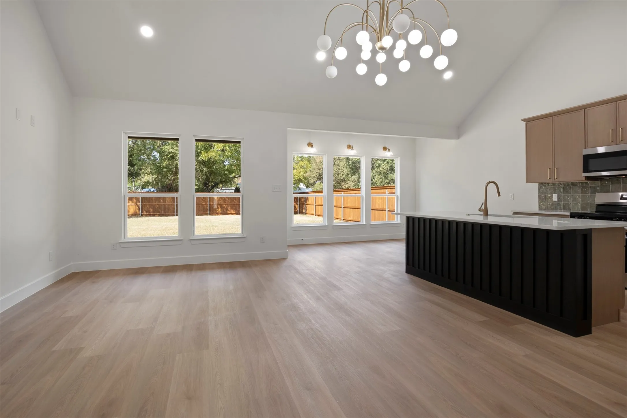 Vaulted ceiling with an orb chandelier, wood-finish flooring, a kitchen island with a white countertop, and expansive windows