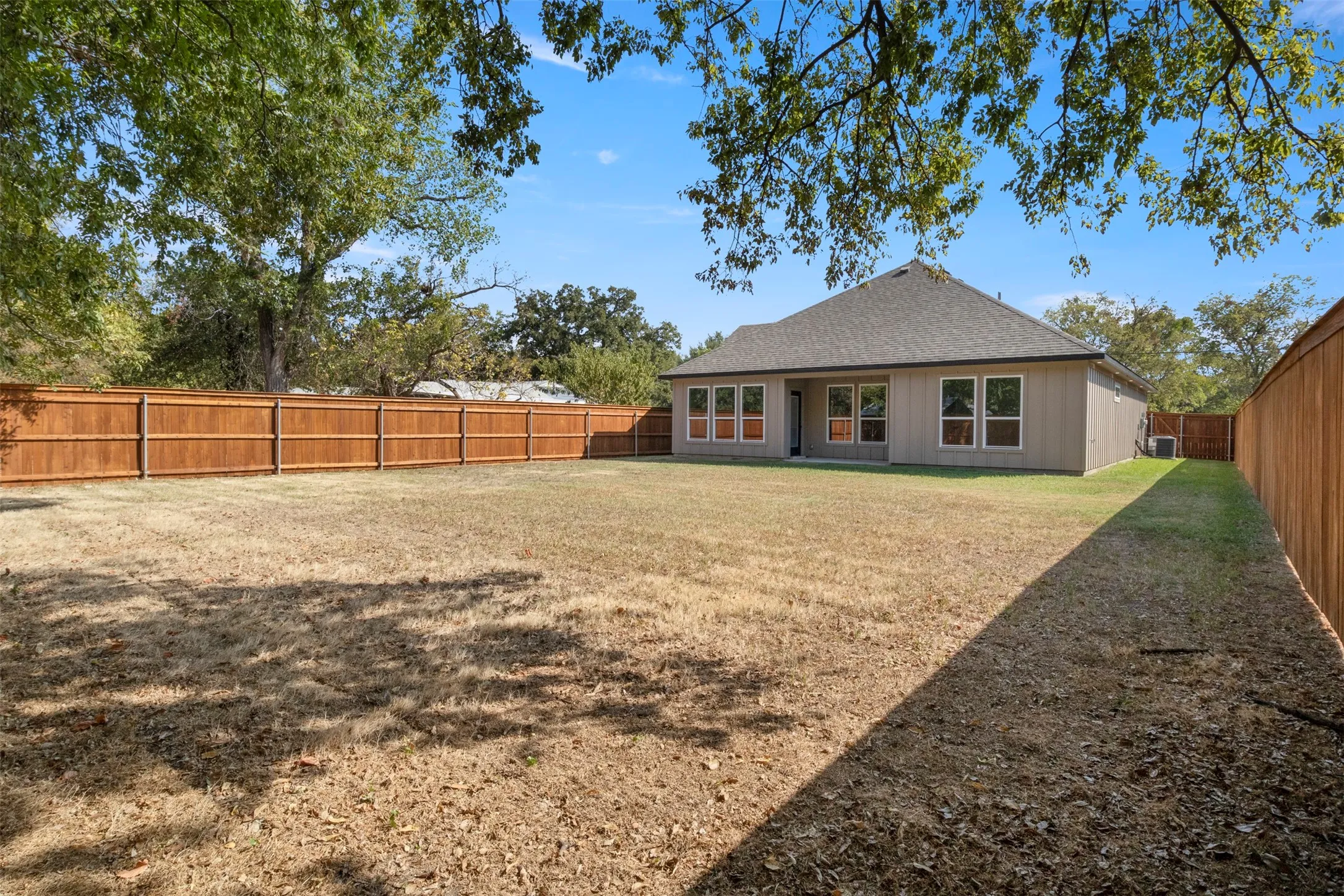 Expansive rear yard with privacy fencing and a detached residential structure featuring a shingled roof and multiple windows