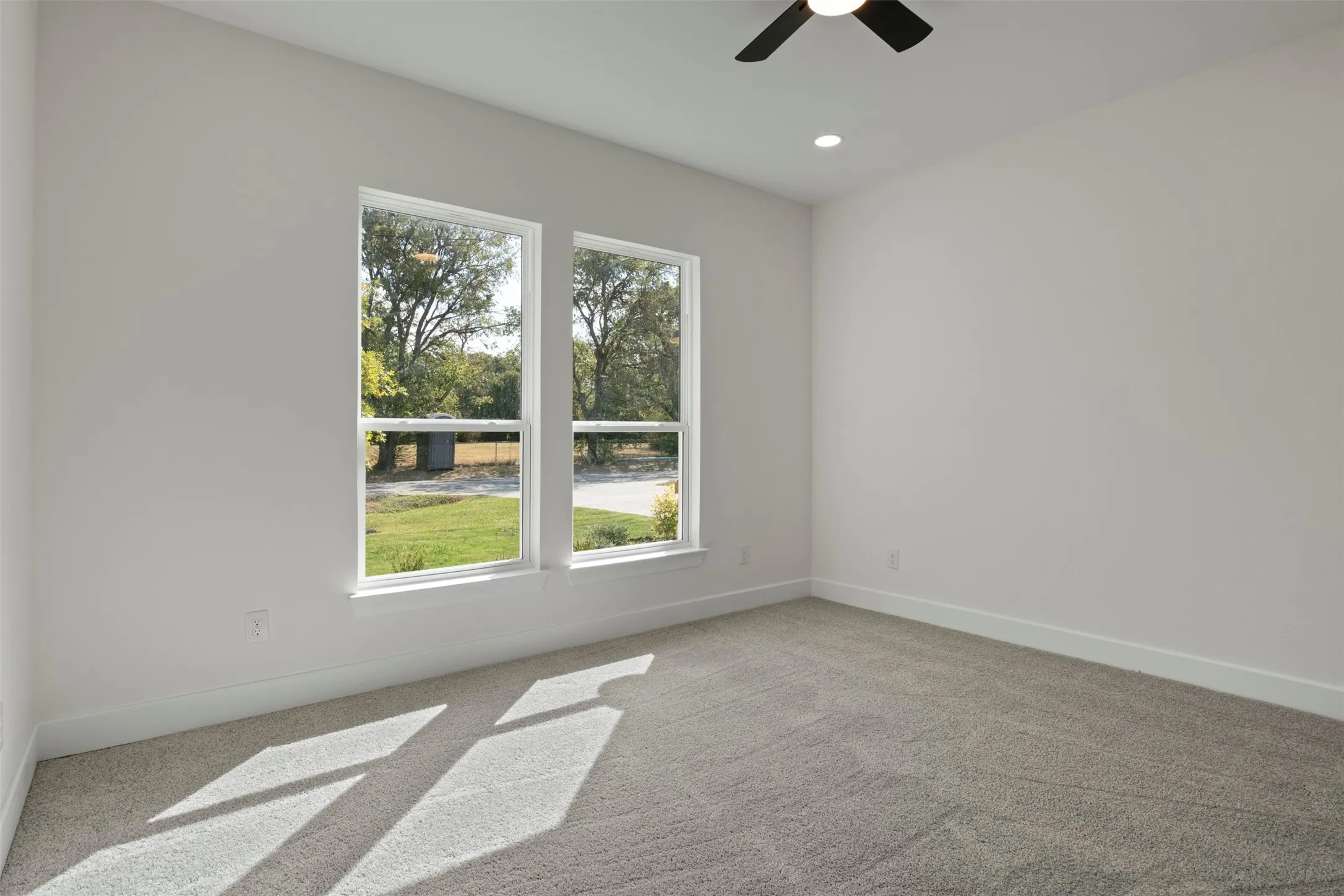 Light gray carpeting, white walls, two windows, recessed lighting, and a ceiling fan