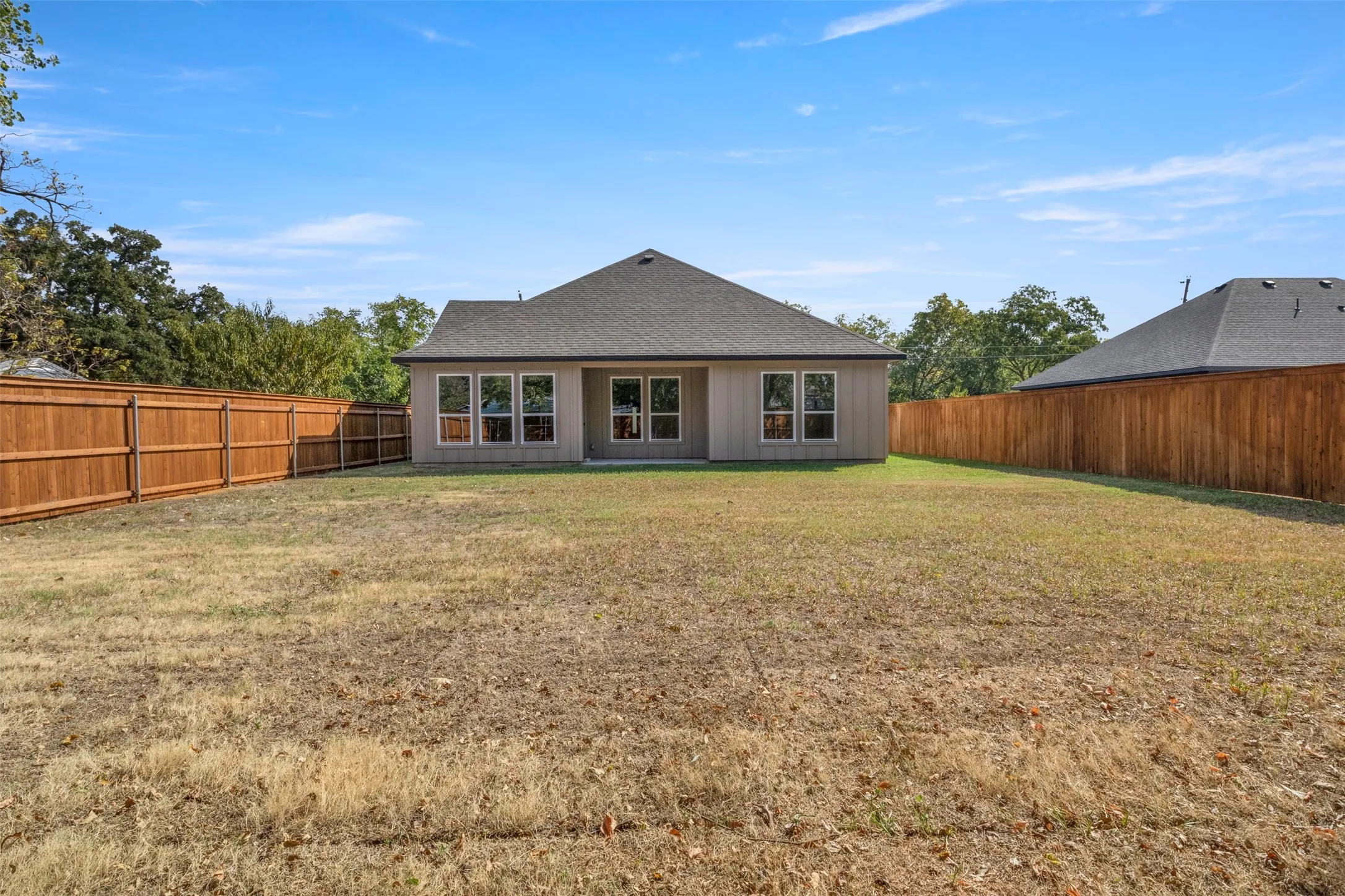 Expansive backyard with a full privacy fence, multiple large windows, and a neutral stucco exterior