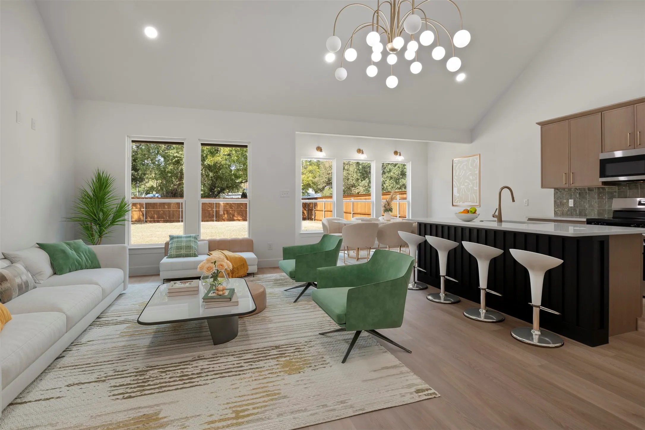 Vaulted ceiling with a contemporary chandelier, light wood-finish flooring, kitchen island with seating, stainless steel appliances, and large windows