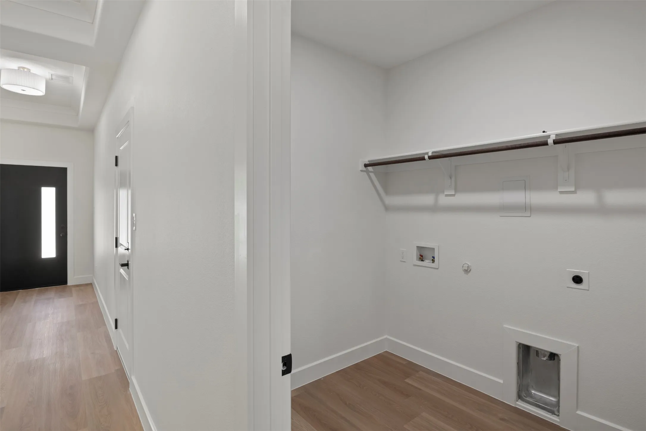 Utility space featuring wood-finish flooring, a clothing rod with shelving, and appliance hookups