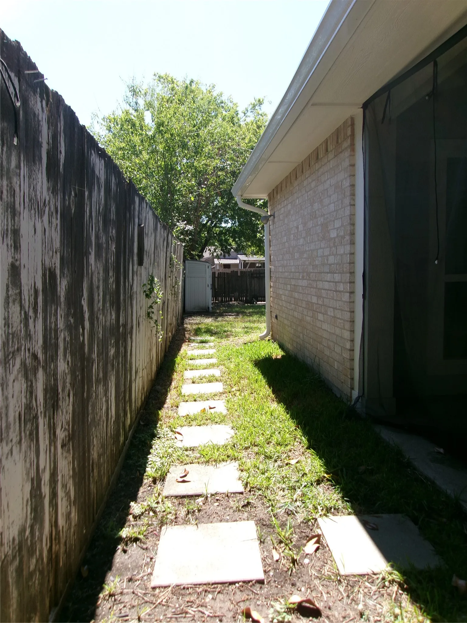 Brick exterior with a screened enclosure, concrete stepping stone pathway, and wood fencing