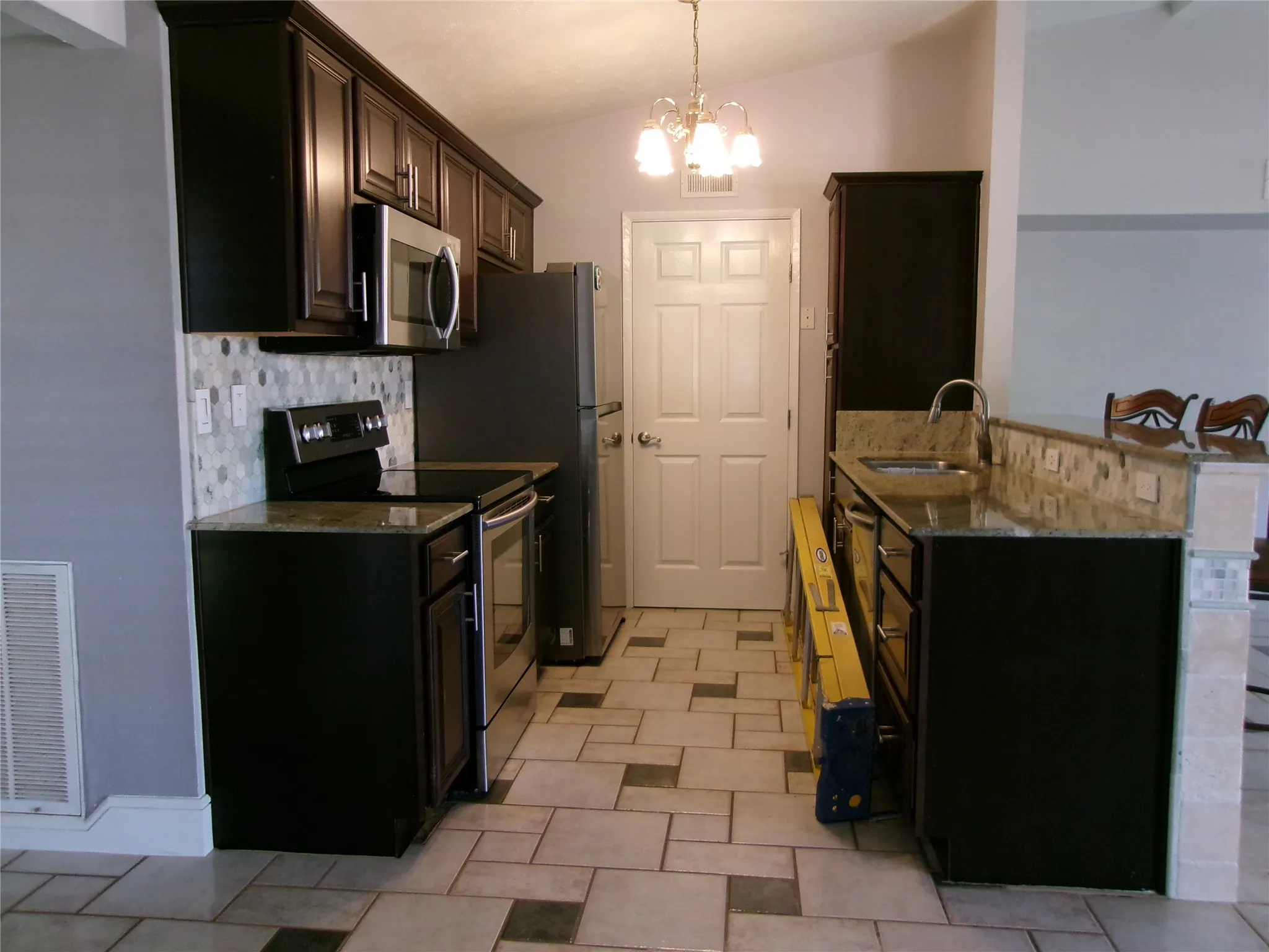 Kitchen featuring dark wood-finish cabinetry, stainless steel appliances, mosaic tile backsplash, and light-toned countertops