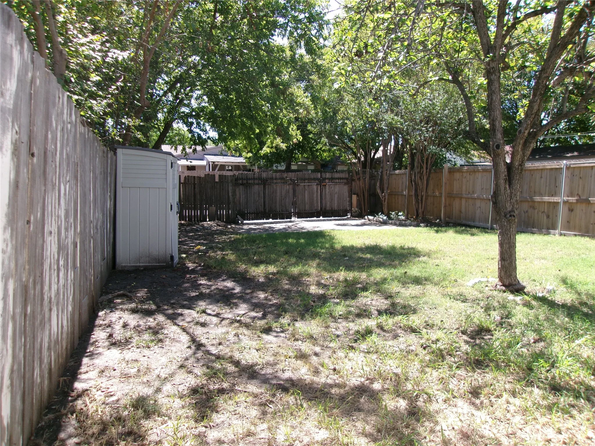 Fenced backyard featuring a storage shed, mature trees, and a grass area