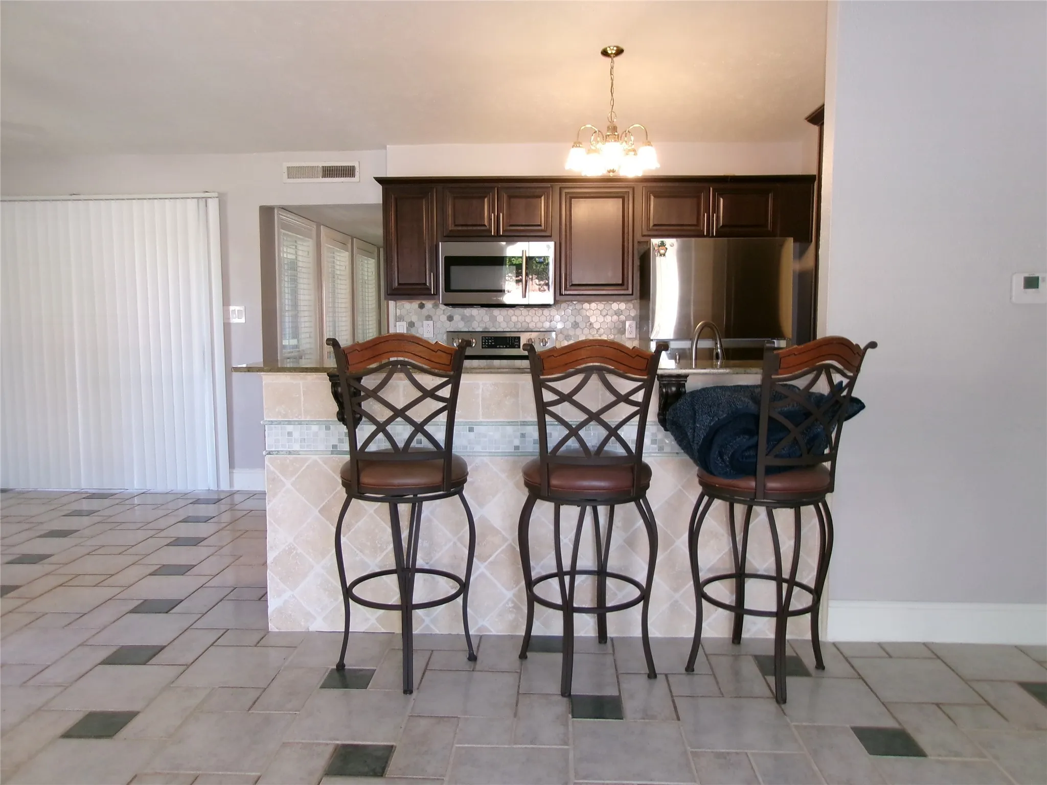 Kitchen featuring dark wood-finish cabinetry, stainless steel appliances, a tiled backsplash, and an island with a breakfast bar