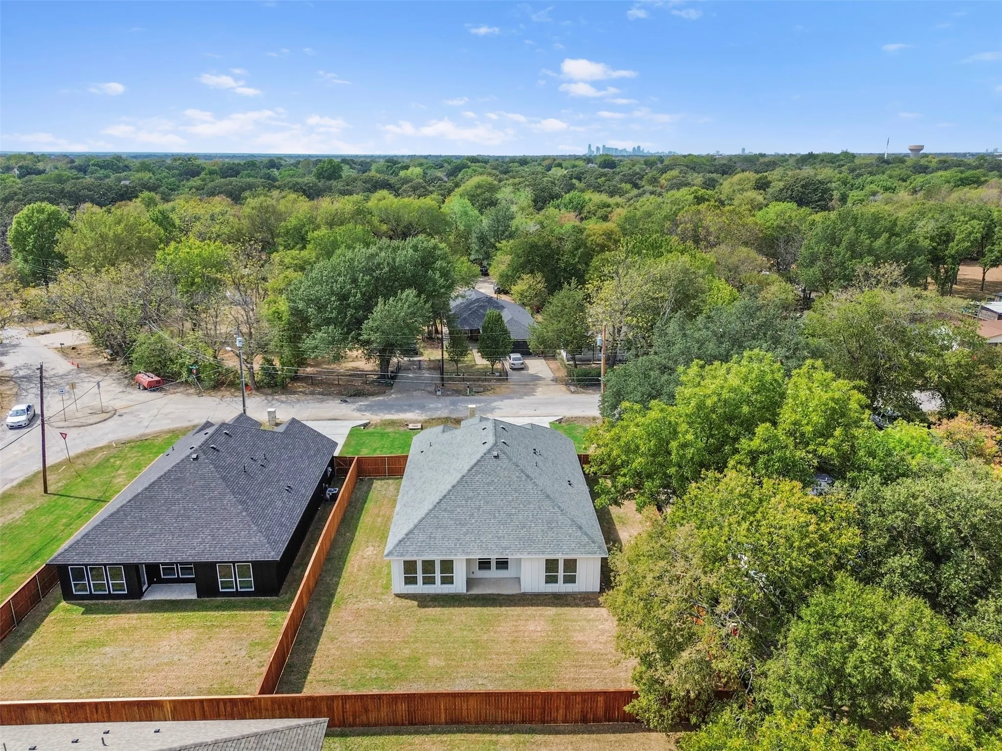 Expansive property featuring a newly constructed residence with a light gray shingle roof, a surrounding wood fence, and a large grass yard