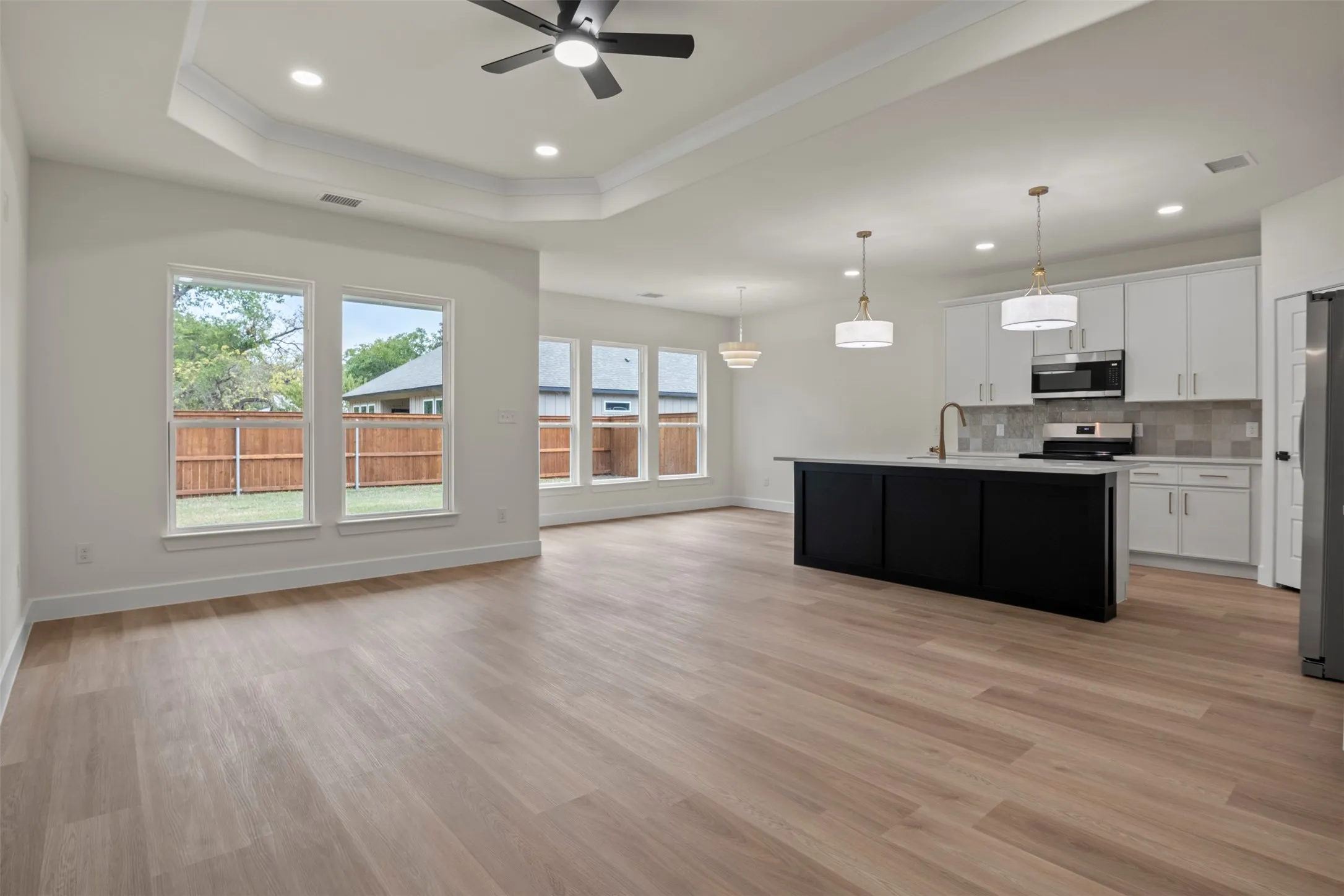 Open-concept living space featuring wood-finish flooring, recessed lighting, and a tray ceiling