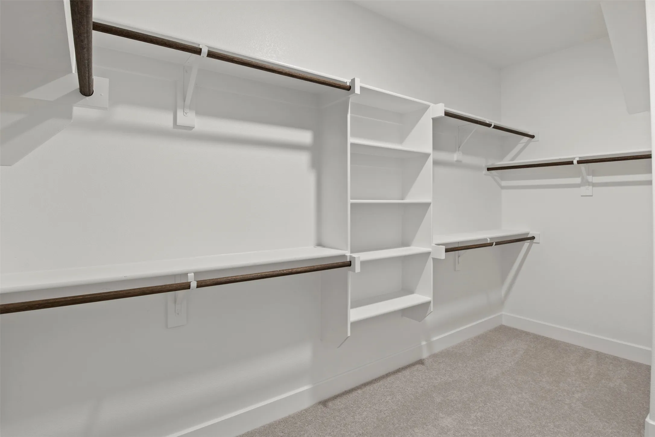 Walk-in closet featuring white built-in shelving, multiple hanging rods, and light-colored carpeting