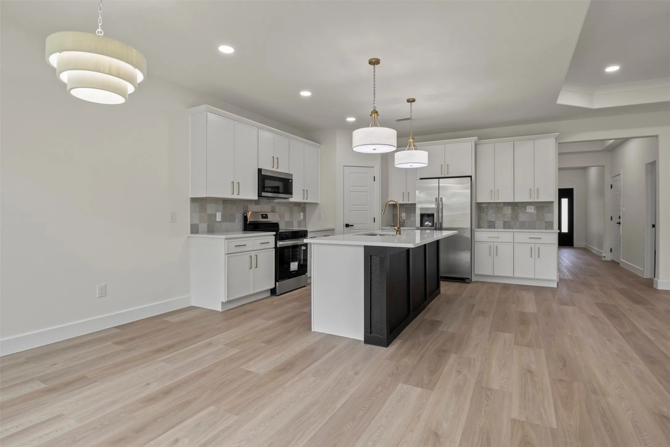 Light wood-finish flooring throughout, white upper and lower cabinetry, stainless steel appliances, a kitchen island with a light-toned countertop, and recessed lighting