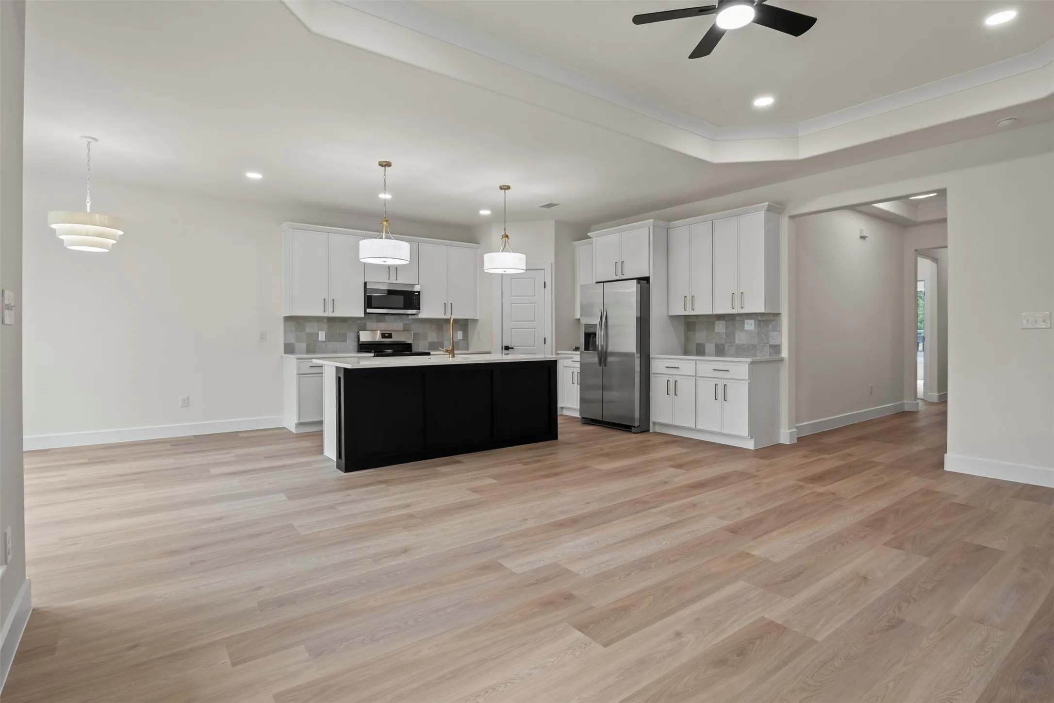 Wood-finish flooring throughout, tray ceiling with recessed lighting, black kitchen island, white cabinetry, and stainless steel appliances