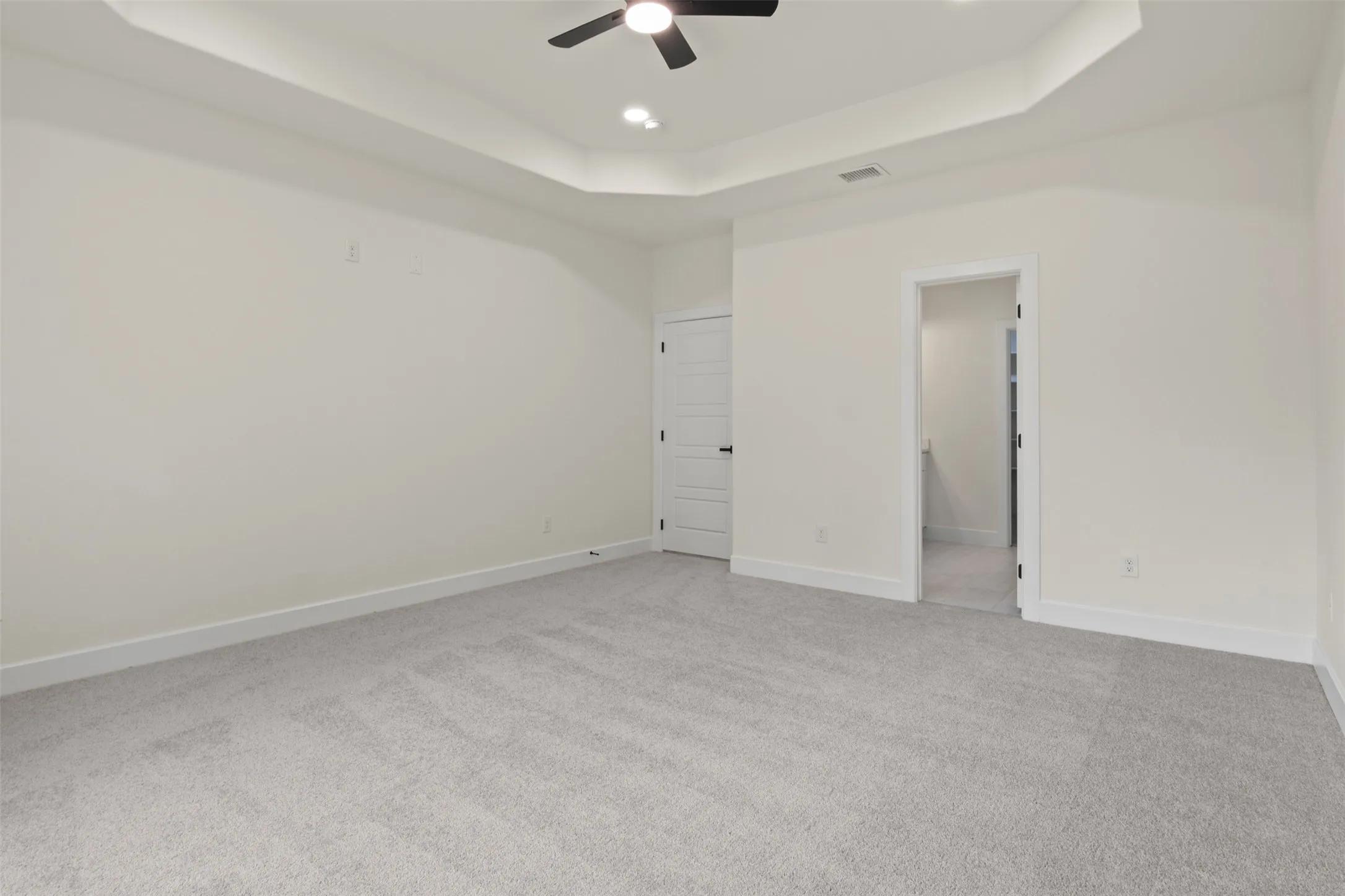 Tray ceiling with recessed lighting and a ceiling fan, light gray carpet flooring, and white trim