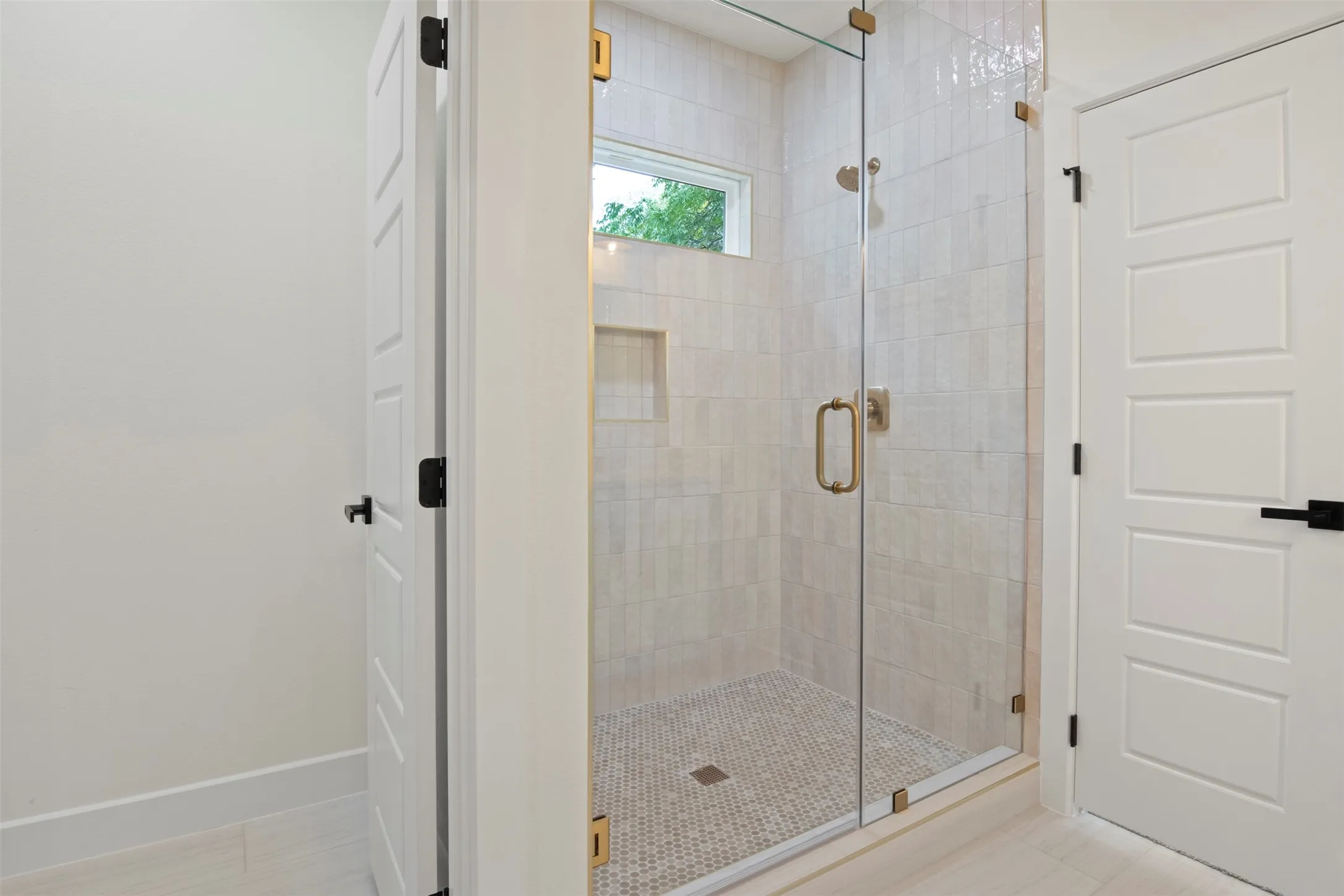 Glass-enclosed shower with gold-tone hardware, a tiled shower niche, and a window