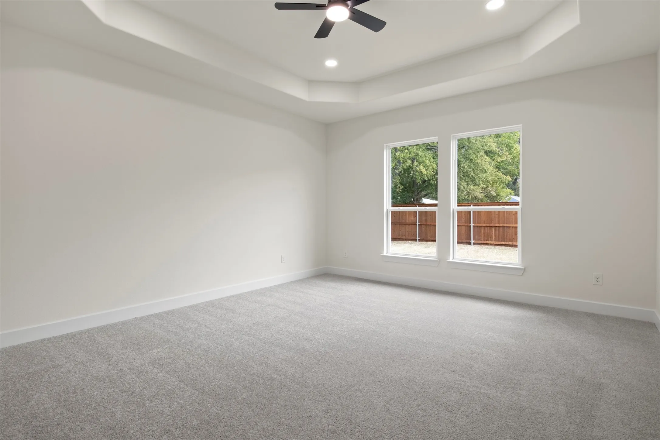 Spacious room featuring a tray ceiling, recessed lighting, and a ceiling fan
