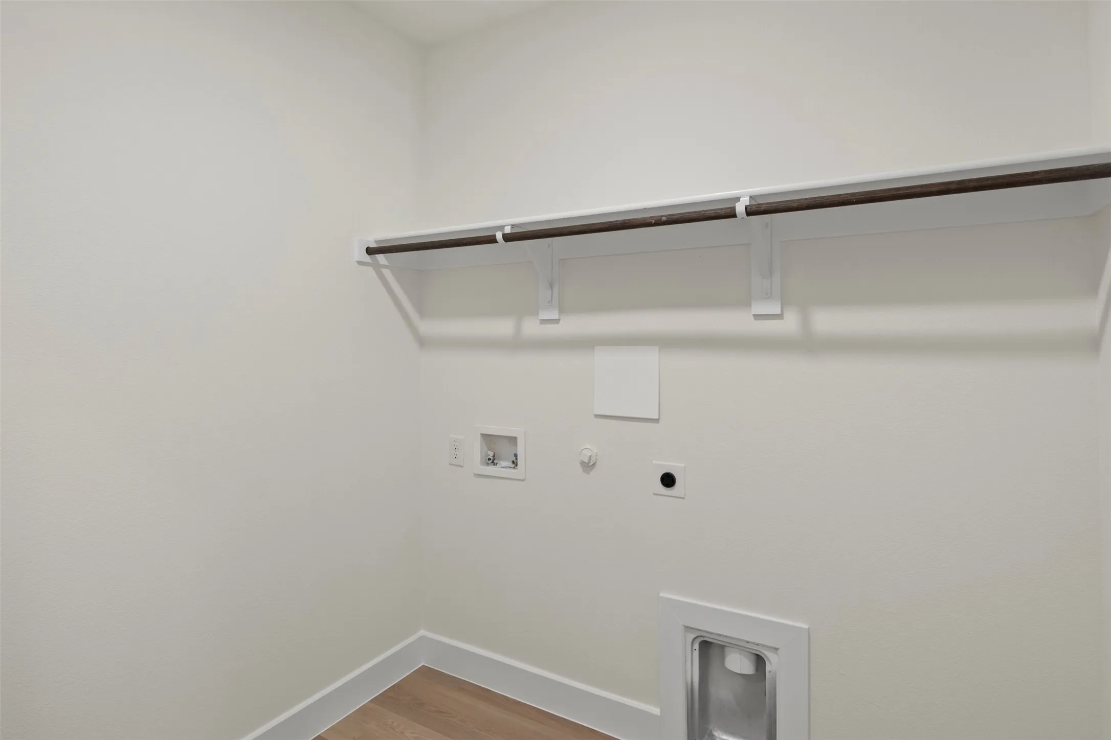Laundry space featuring a hanging rod, utility connections, and wood-finish flooring