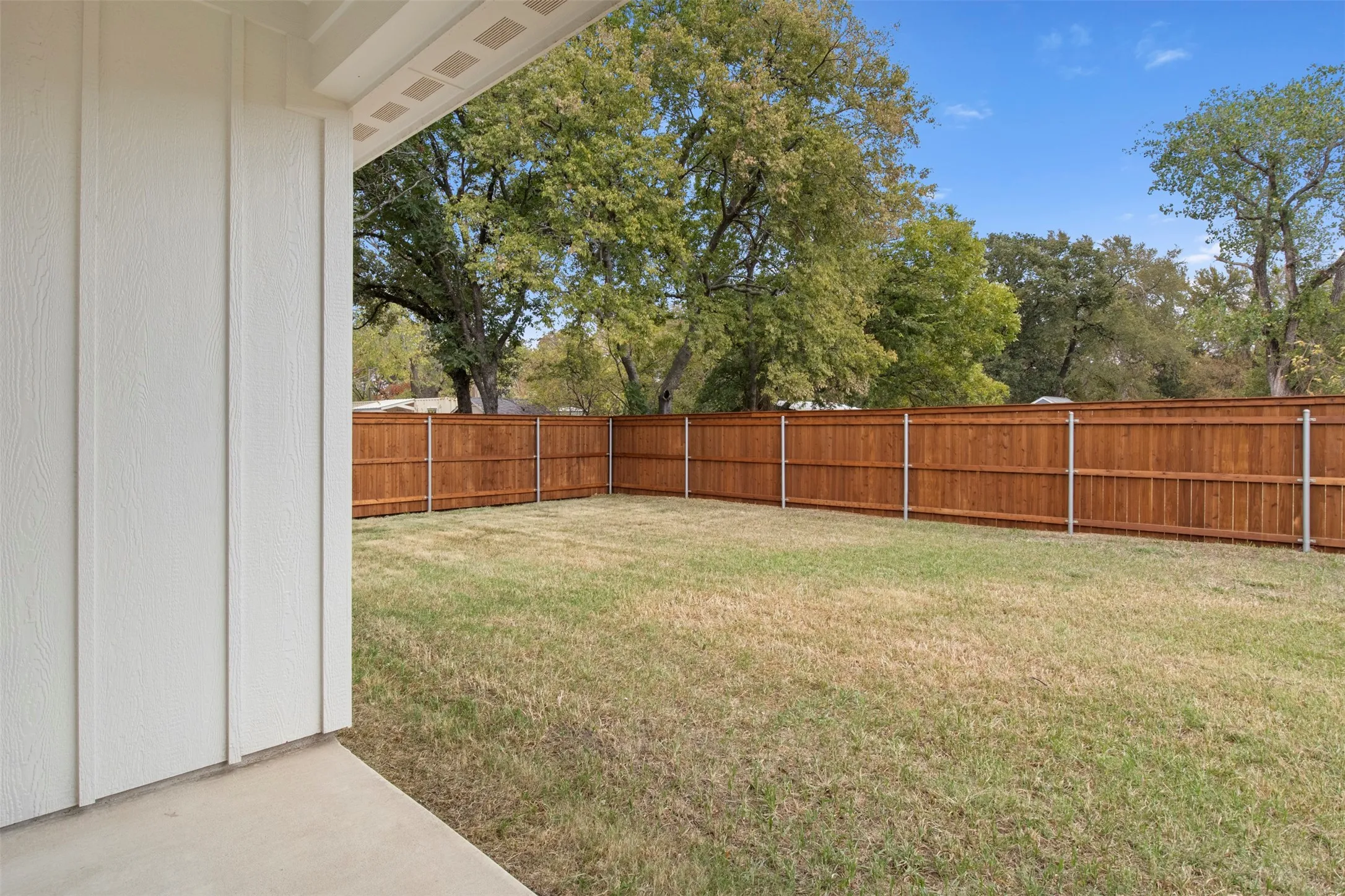 Expansive backyard featuring a stained wood privacy fence, concrete patio, and mature trees