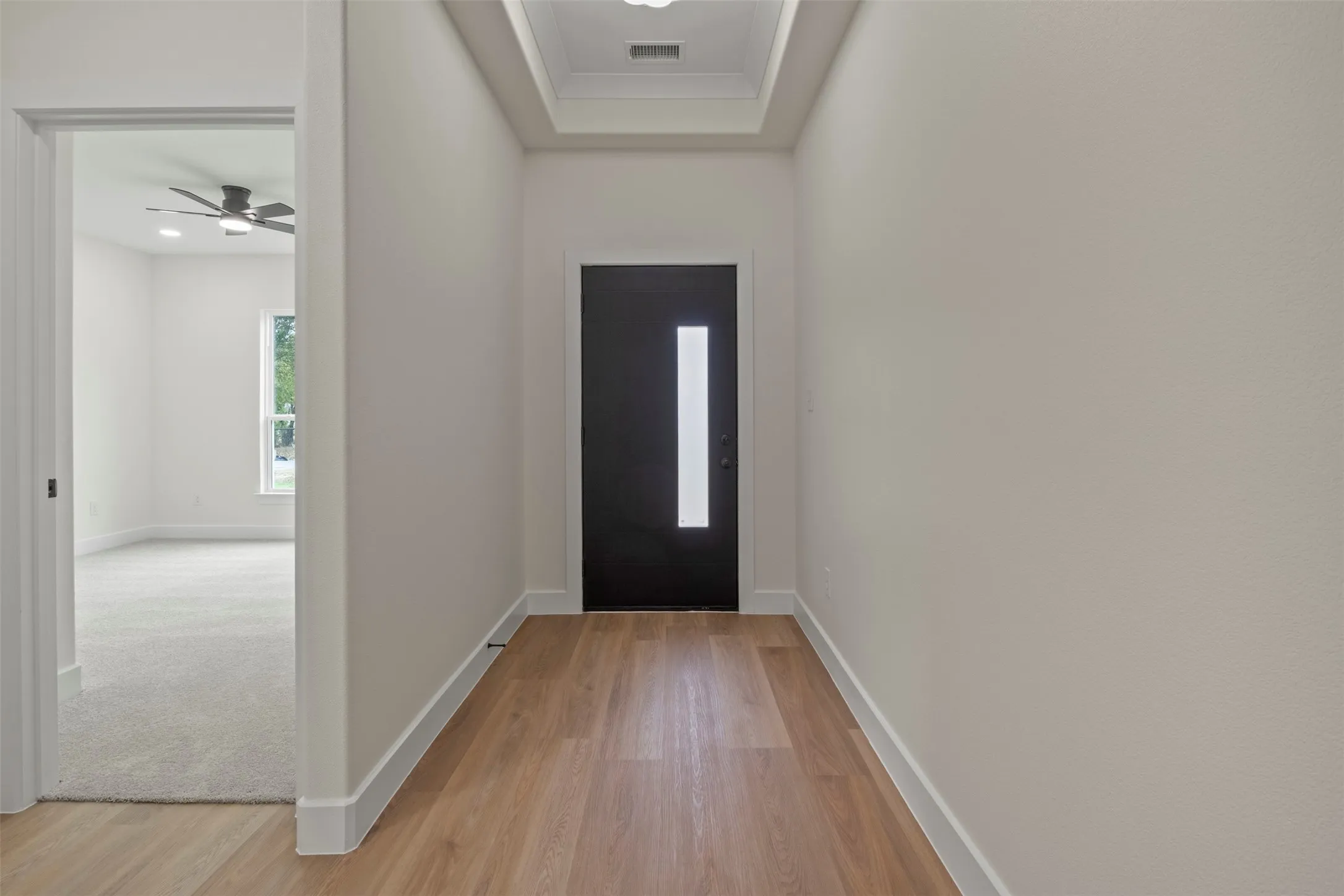 Recessed lighting, wood-finish flooring, tray ceiling, black front door with vertical pane, and light grey carpeting