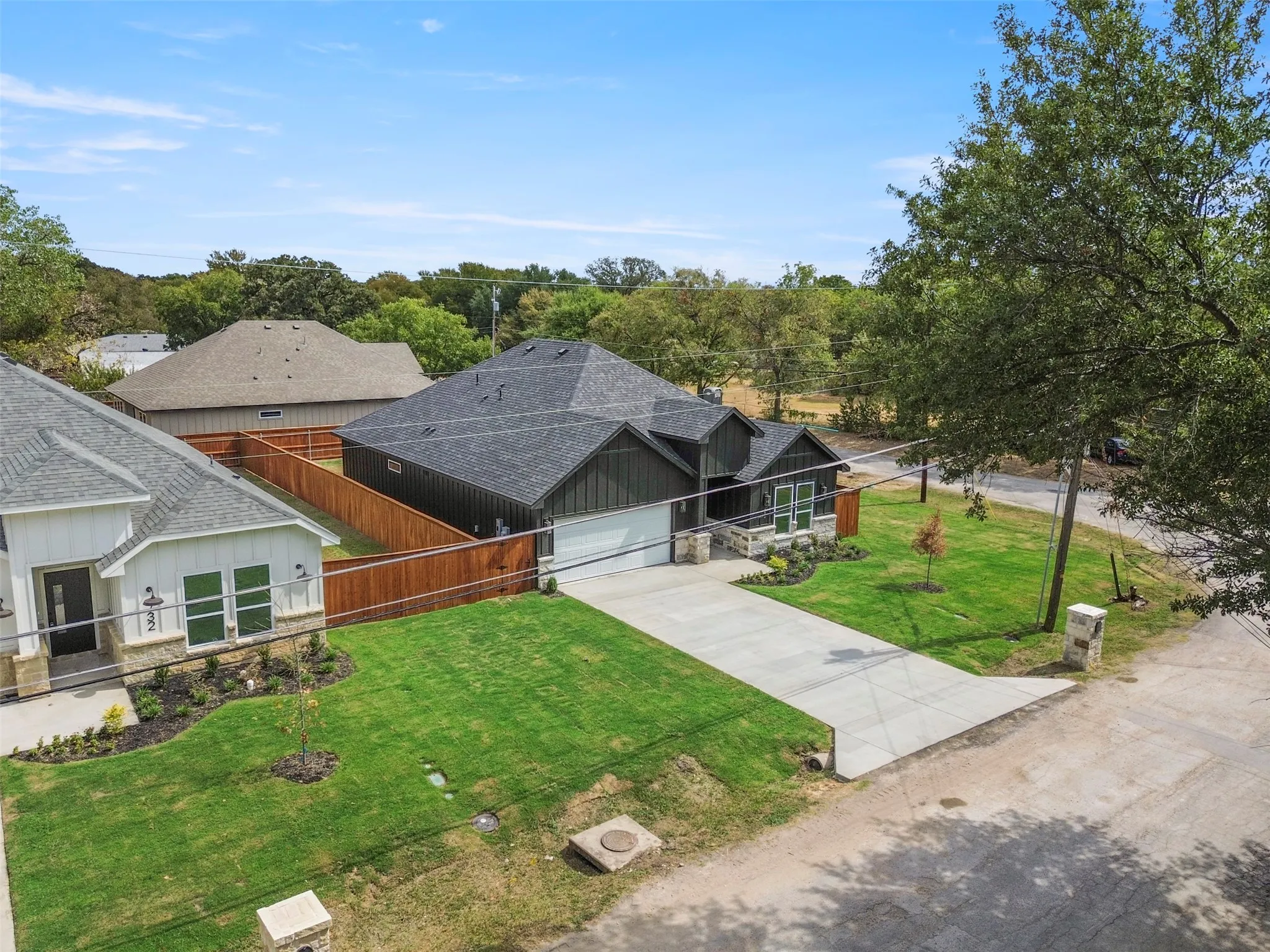 Contemporary home featuring a dark shingle roof, stone accents, a concrete driveway, and a wooden privacy fence