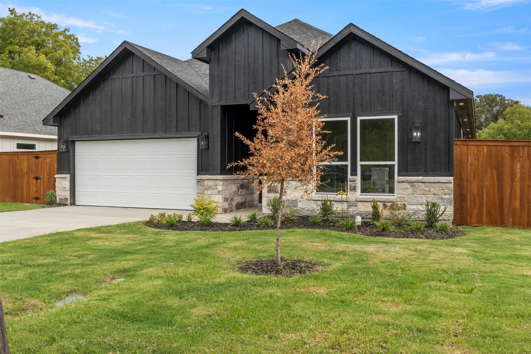 Modern black exterior with stone accents, a white garage door, and a manicured lawn