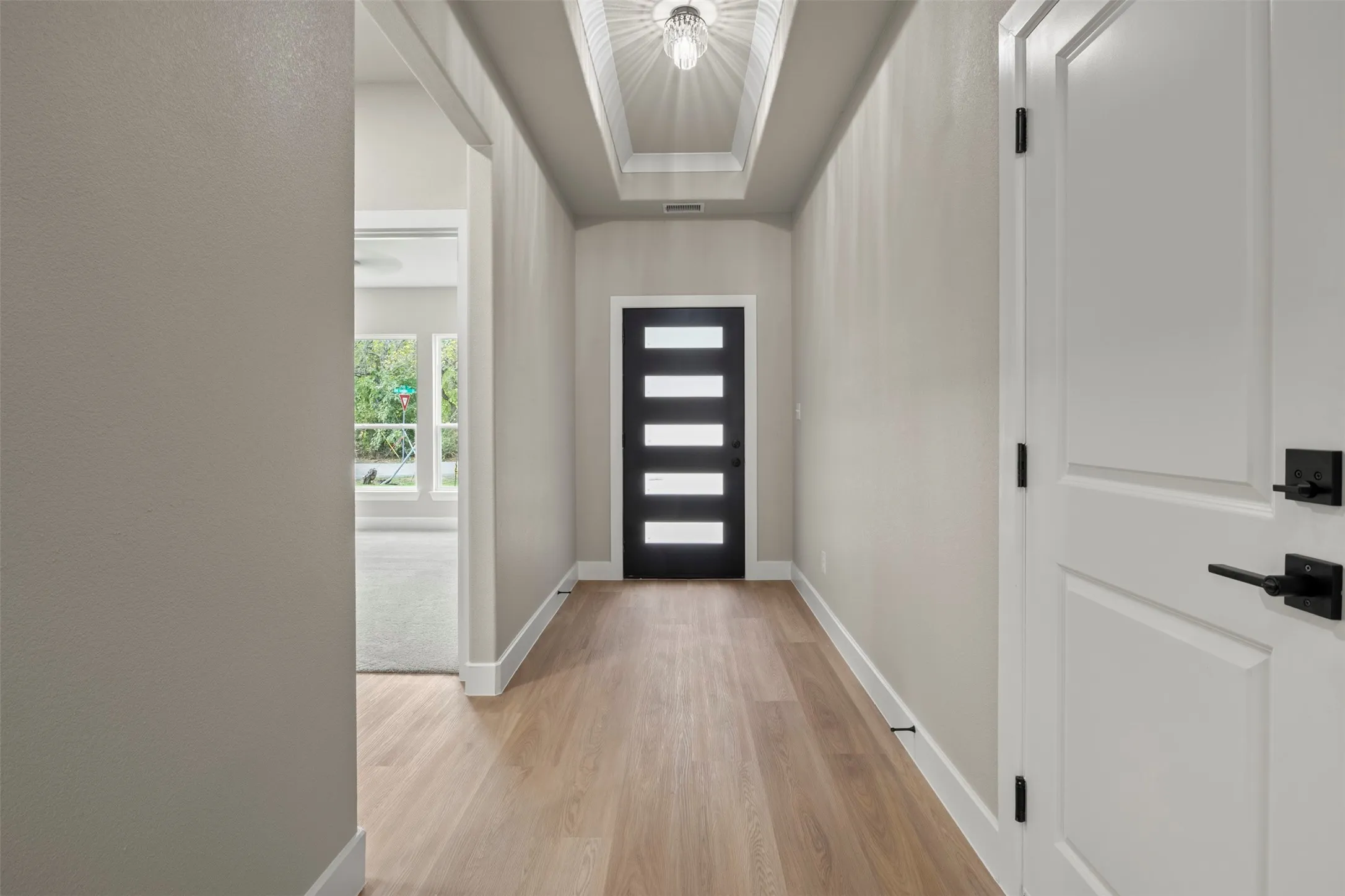 Modern front door with frosted glass panels, wood-finish flooring, and a tray ceiling with recessed lighting