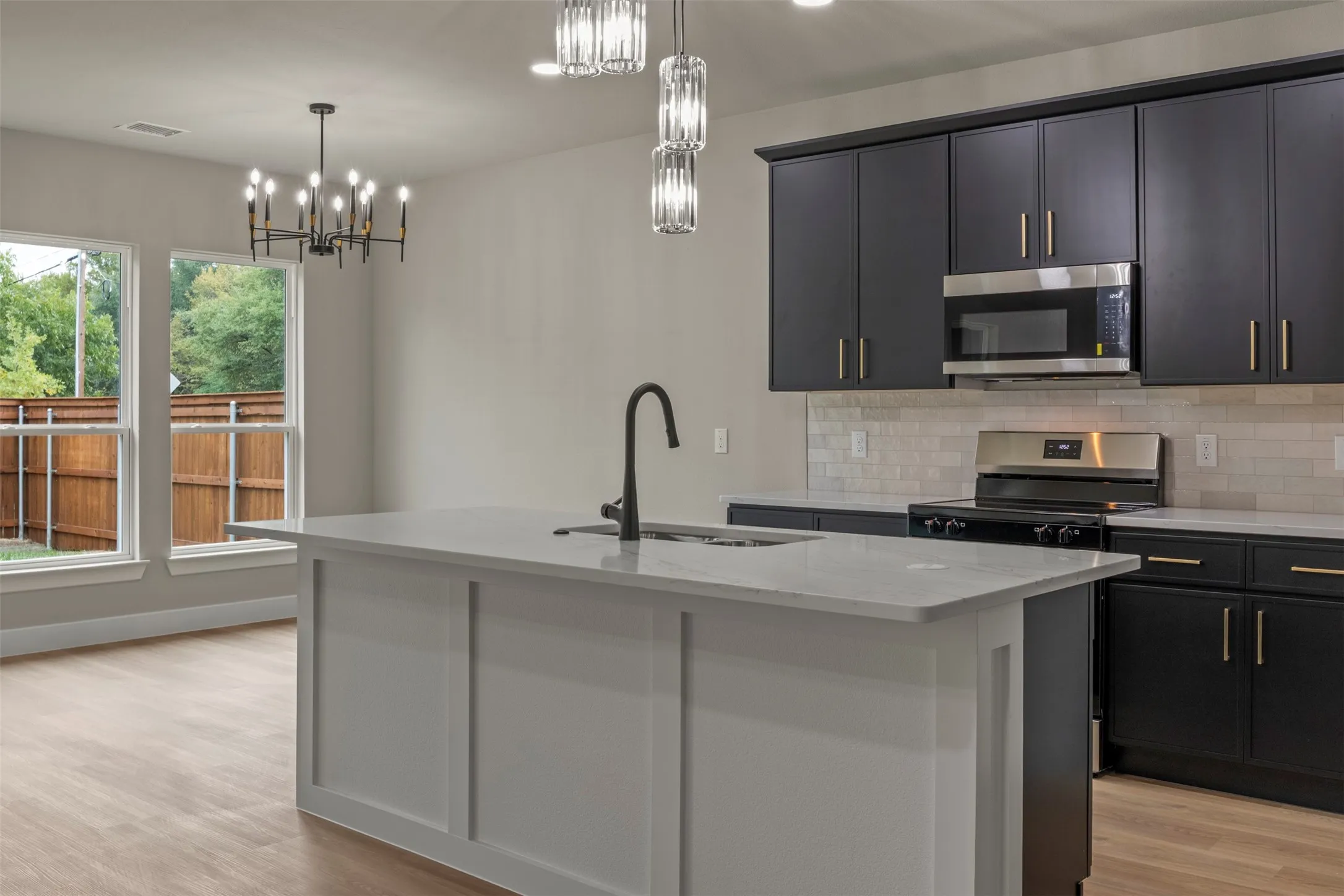 Kitchen featuring a center island with a sink, black cabinetry, stainless steel appliances, a tile backsplash, and wood-finish flooring