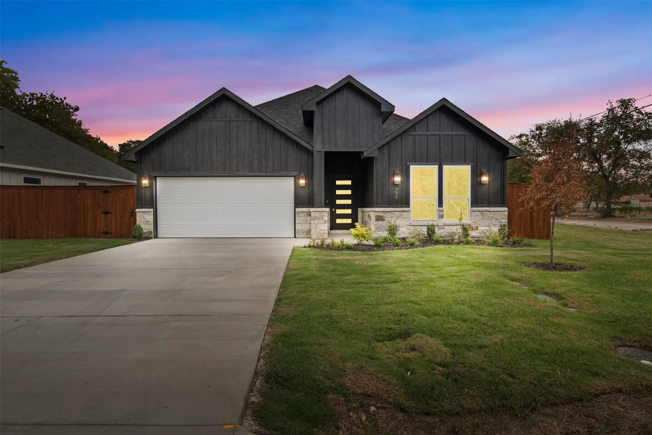 Contemporary exterior featuring dark vertical siding, stone accents, a concrete driveway, and an attached garage