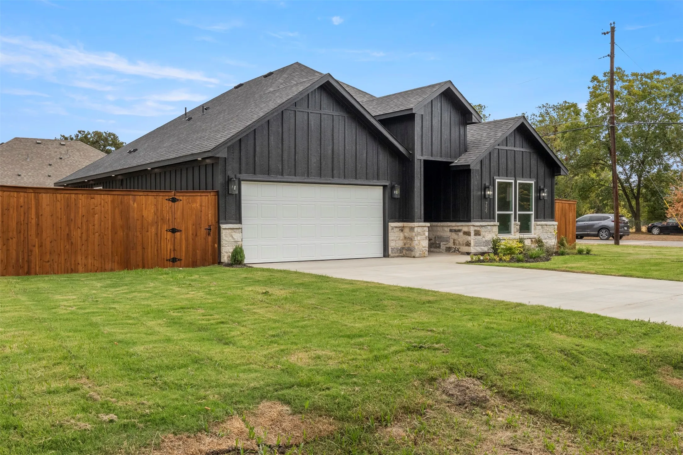 Modern facade featuring black vertical siding, stone accents, a two-car garage, and a concrete driveway