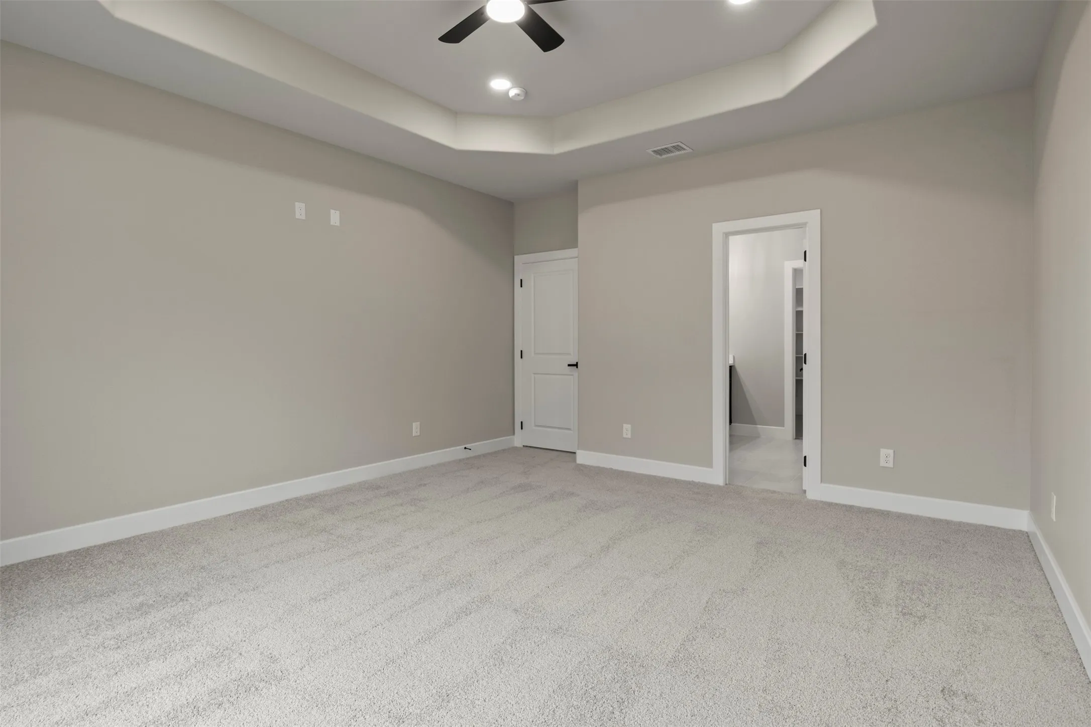 Tray ceiling with recessed lighting and a ceiling fan, light-colored carpet, and white trim