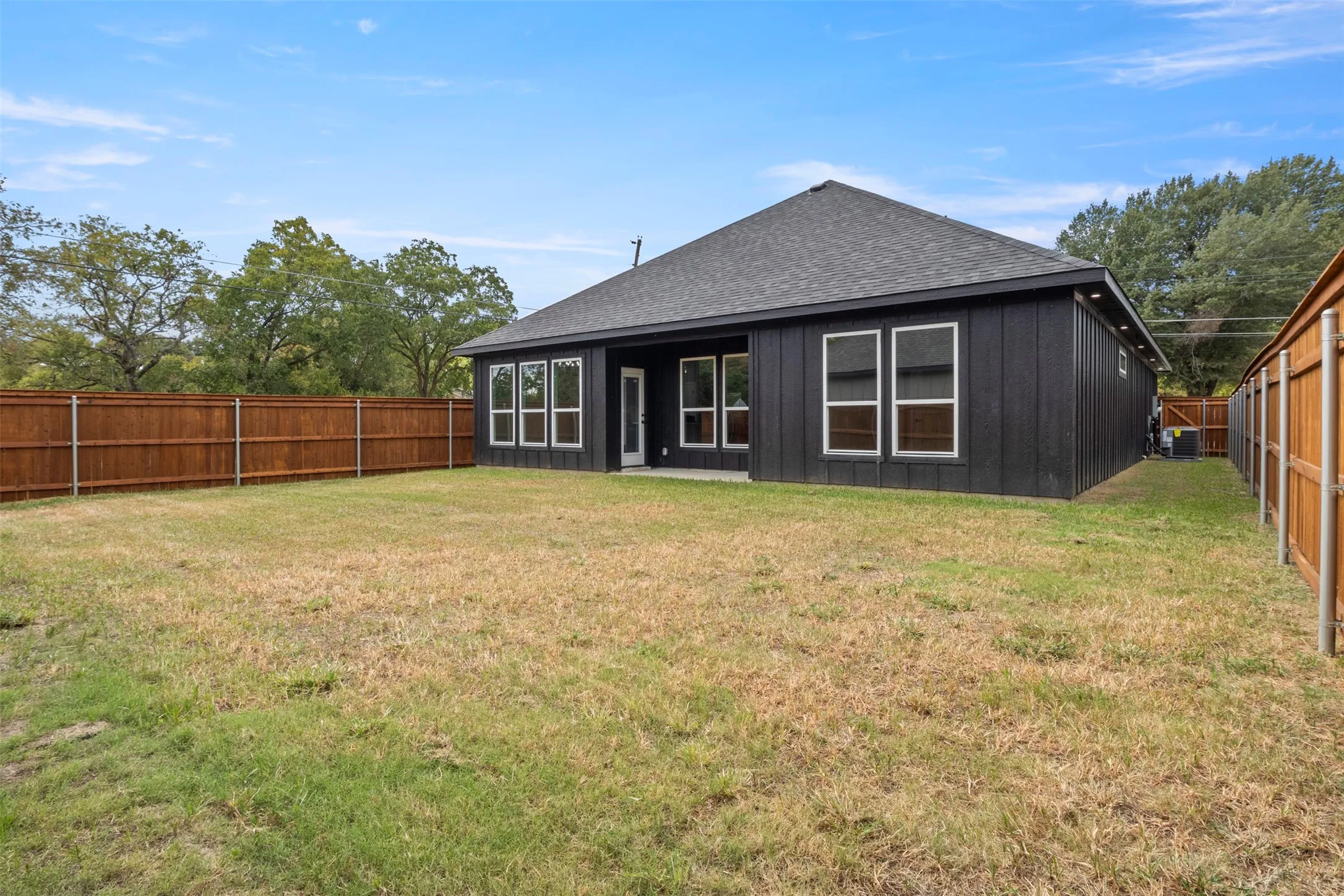 Expansive backyard with a wood privacy fence, dark vertical siding, and multiple windows