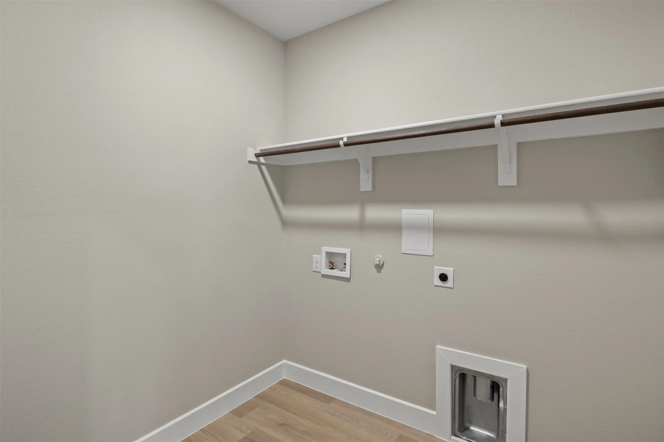 Laundry area featuring a hanging rod, integrated shelving, and wood-finish flooring