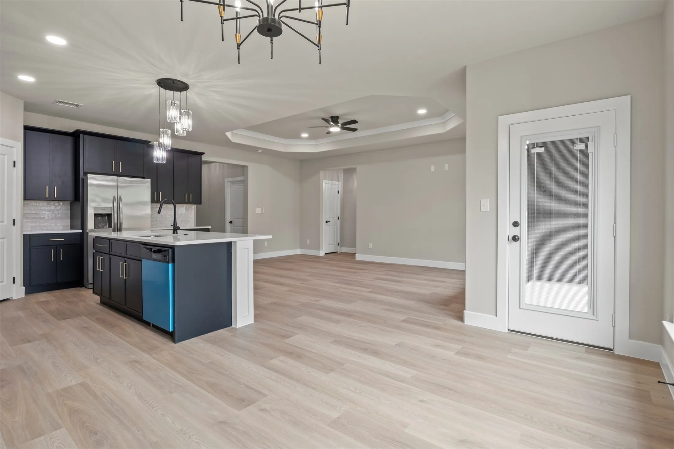 Open-concept living area with wood-finish flooring, a kitchen island, recessed lighting, and a tray ceiling