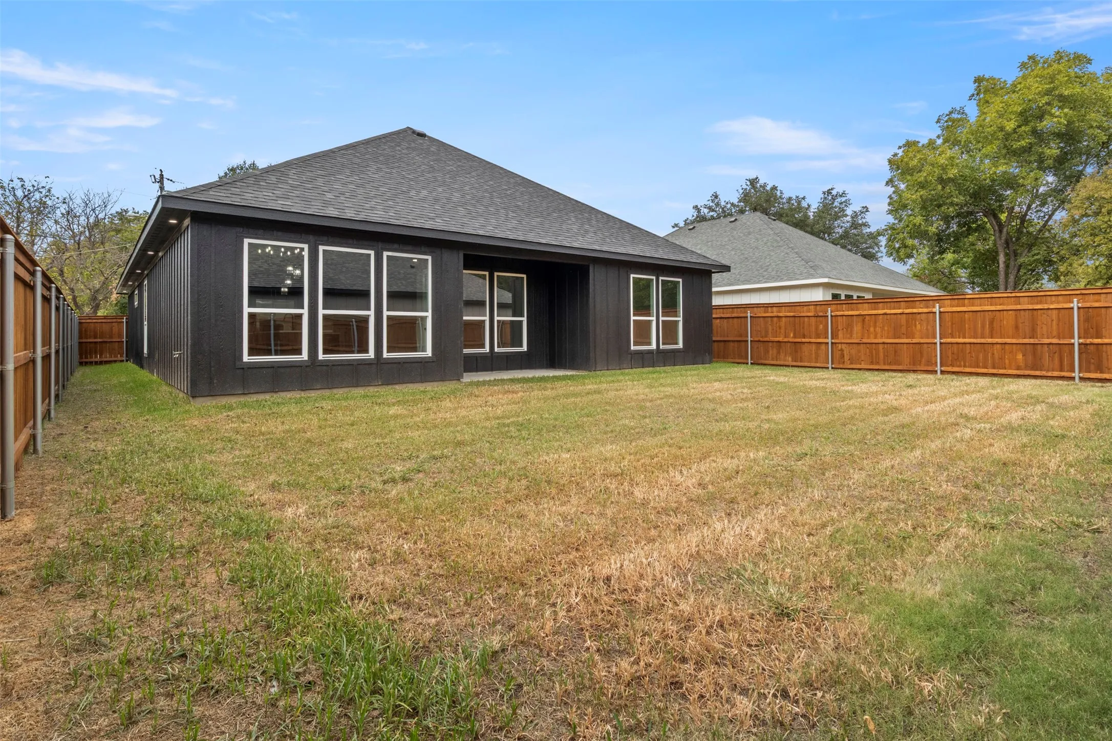 Private fenced backyard featuring a dark wood-sided exterior, a gray shingle roof, and multiple large windows
