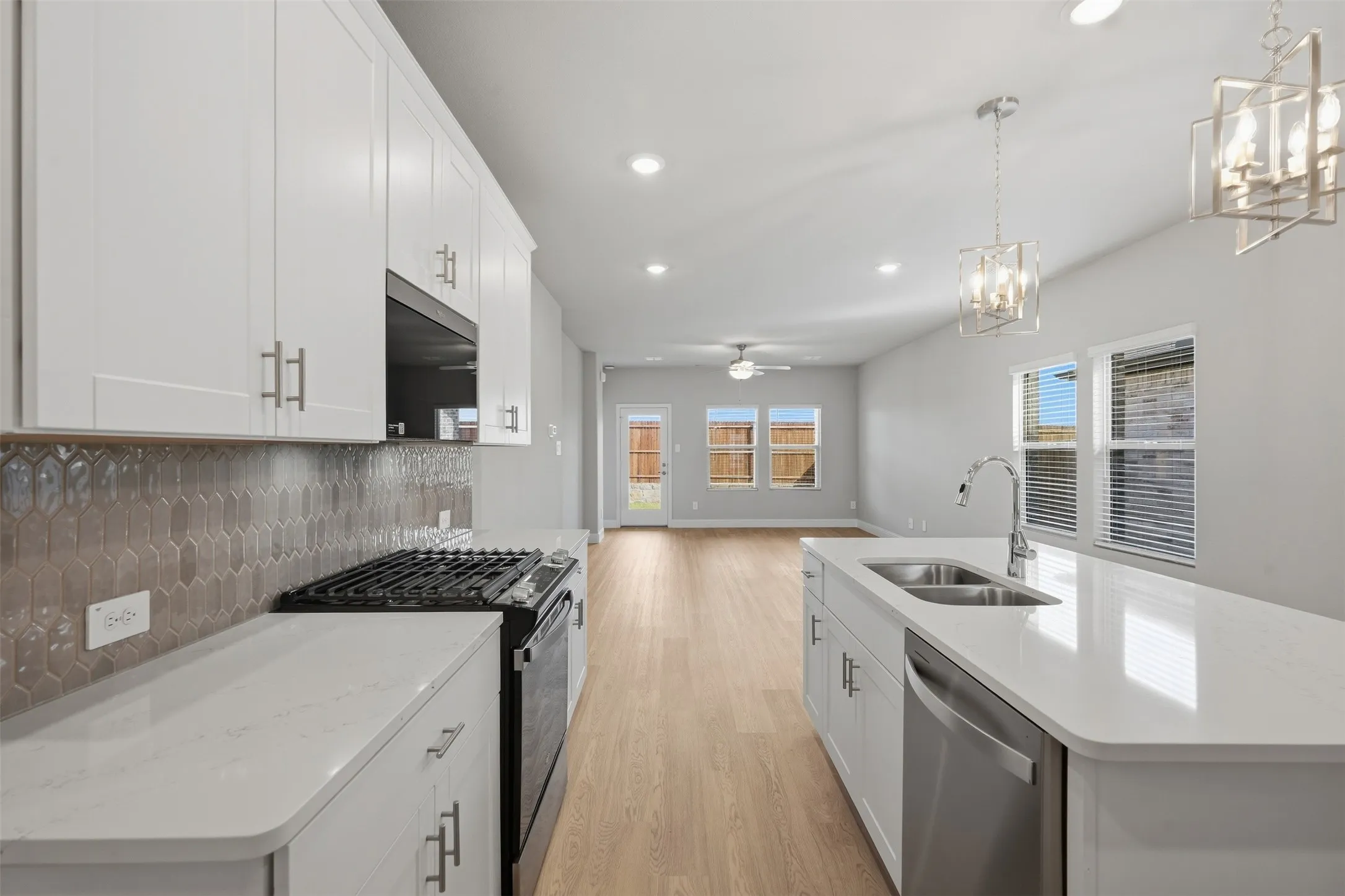 Kitchen featuring white cabinetry, light-toned wood-finish flooring, a stainless-steel sink, an integrated dishwasher, and pendant lighting fixtures